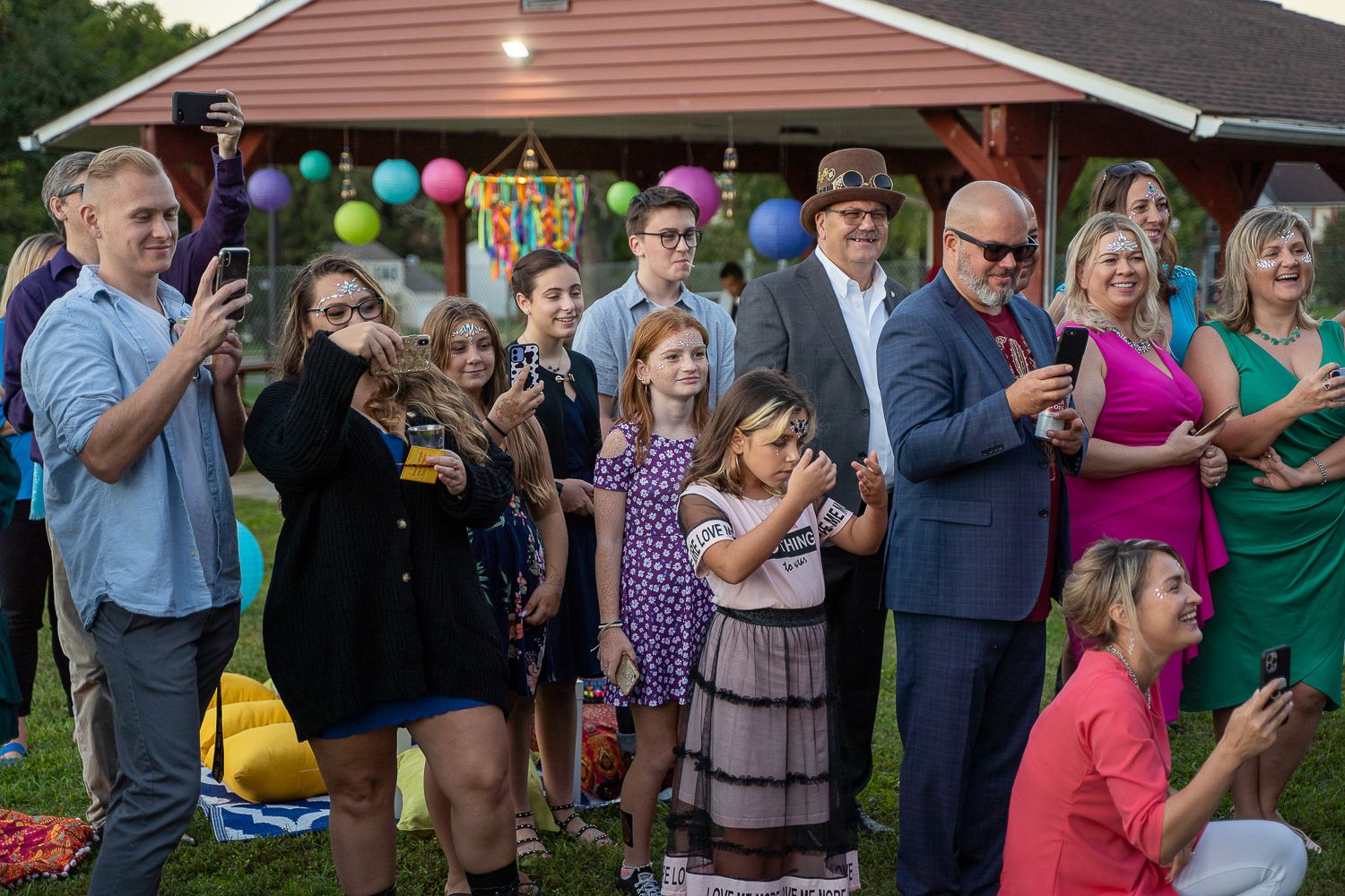 Wedding guests smile and take photos at outdoor evening celebration with colorful balloon decorations in background.