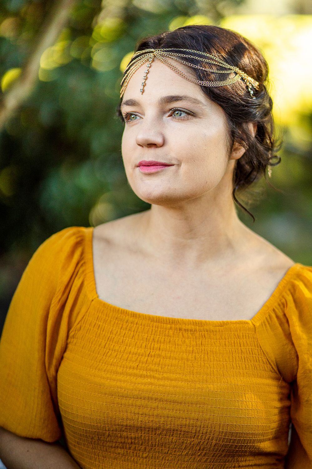 Portrait of young woman in yellow dress wearing gold chain headpiece in natural light.