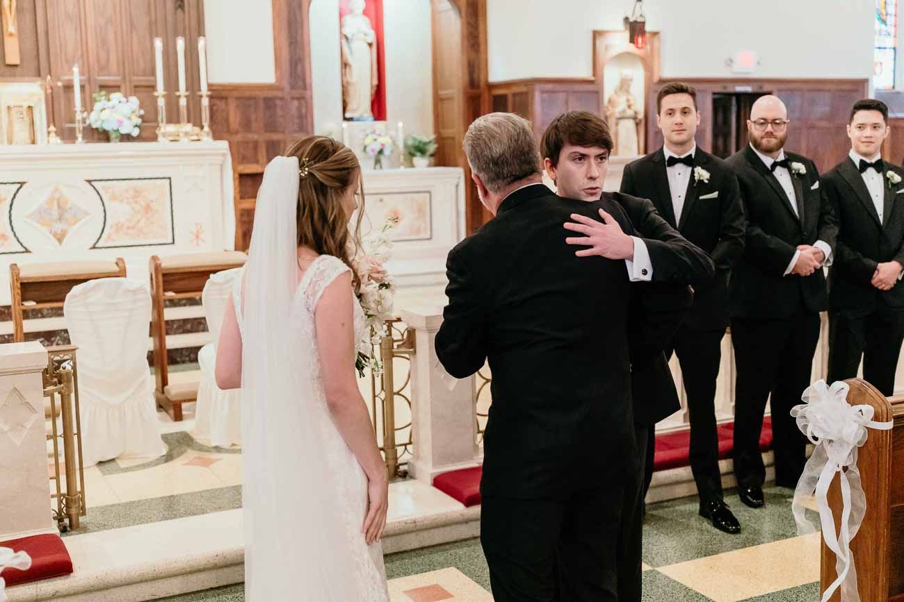 Father of the bride shares an emotional moment with groom at the church altar during ceremony.