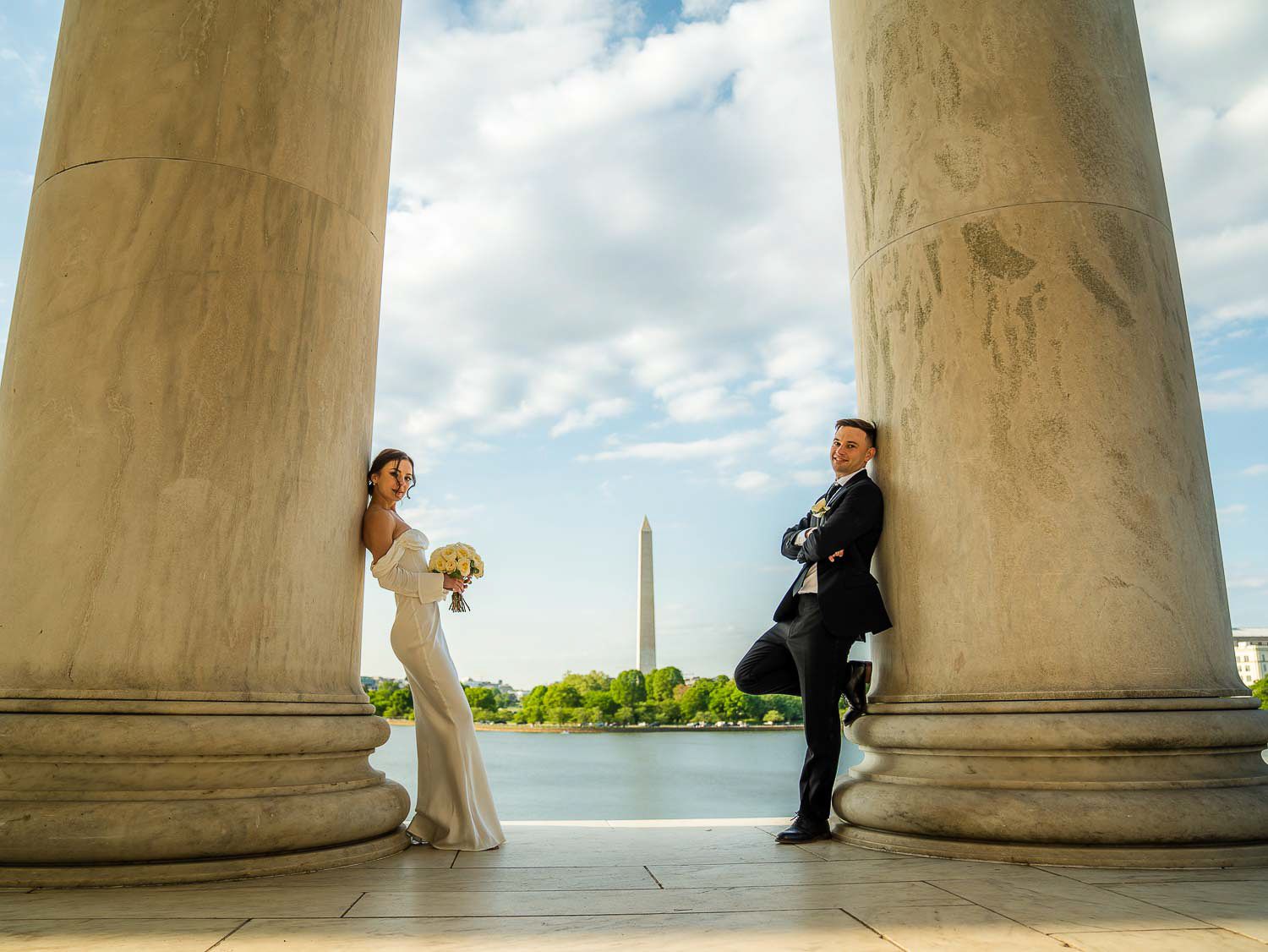 Bride and groom pose between grand columns with the Washington Monument in the background.