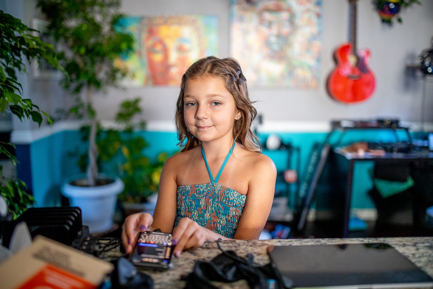 Young girl in teal dress sitting at table holding small box in colorful room.