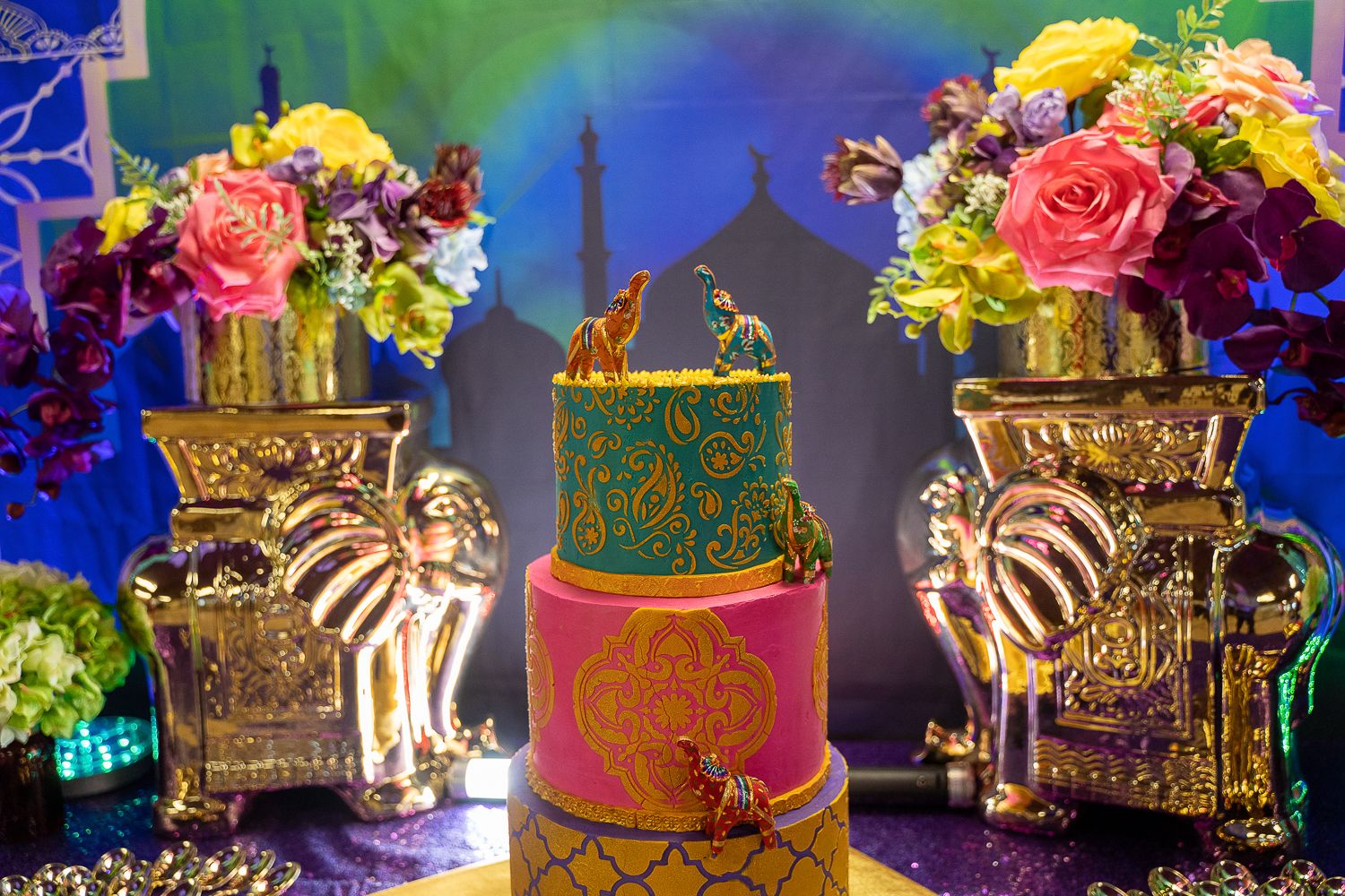 Exotic Arabian Nights birthday cake with gold elephant decorations and vibrant floral arrangements in golden vases.