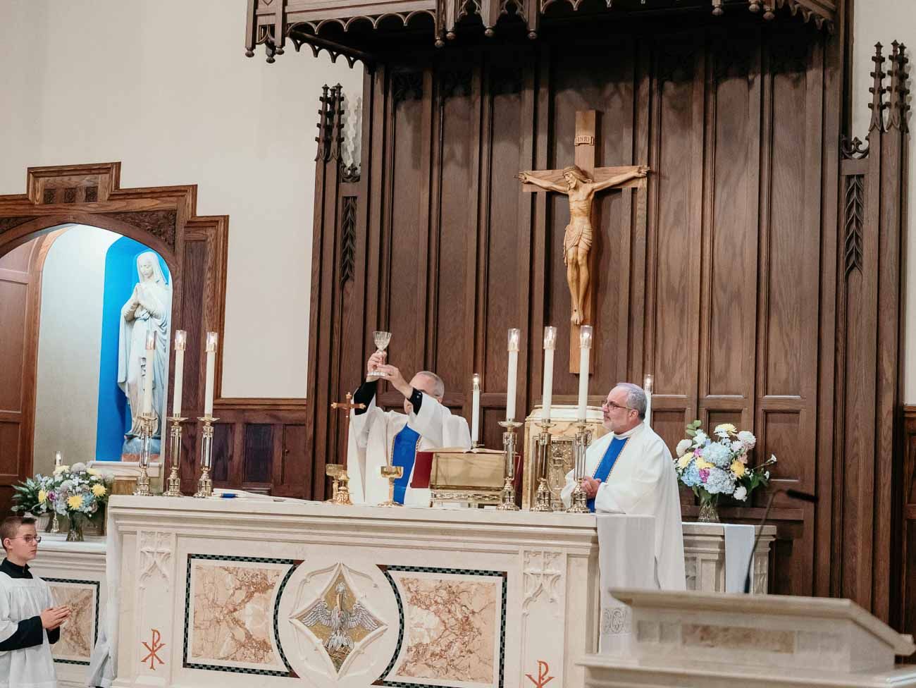 Catholic priest elevates the Eucharist at an ornate altar during a wedding Mass ceremony.