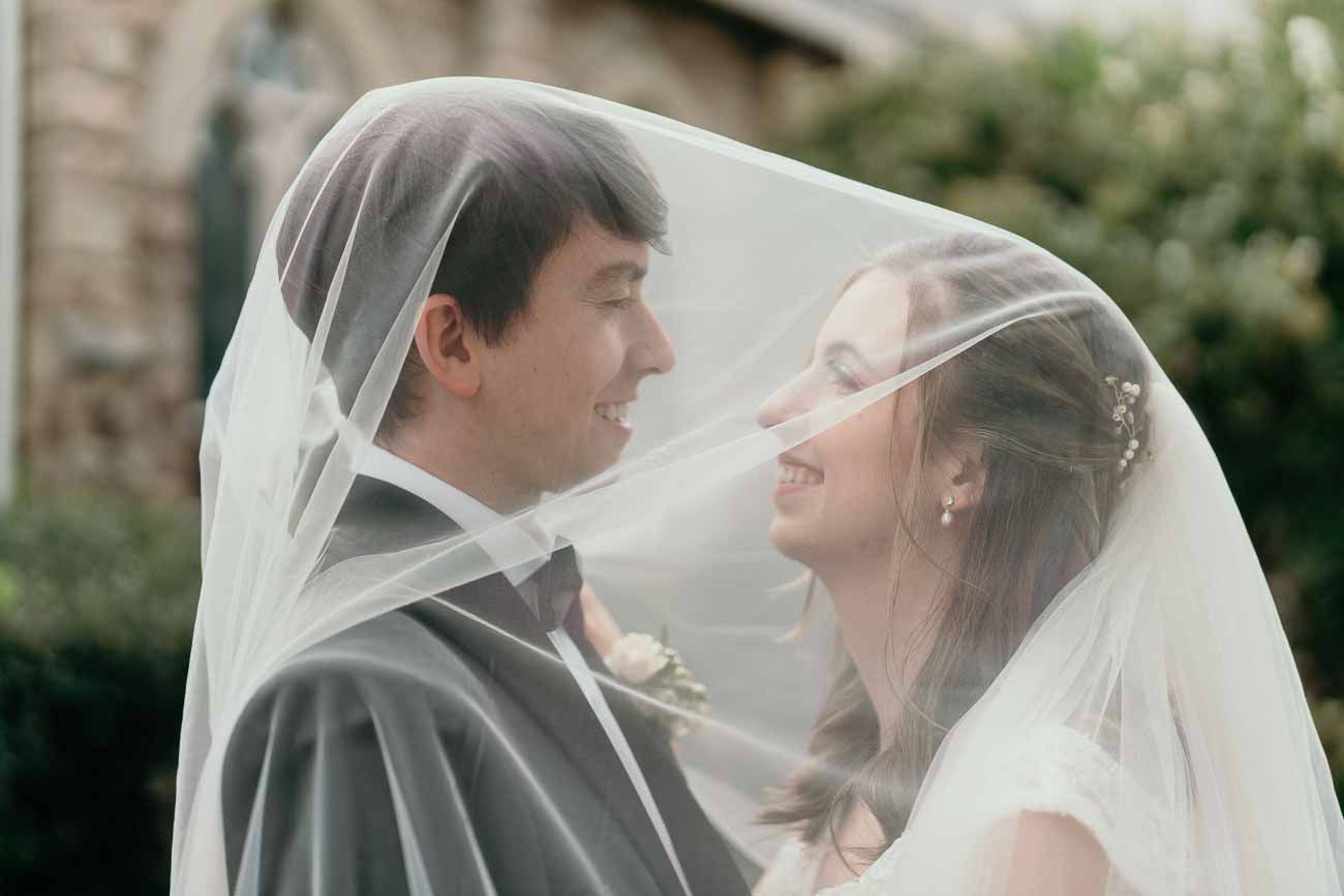 Bride and groom share a tender moment together beneath the bride's flowing white wedding veil.