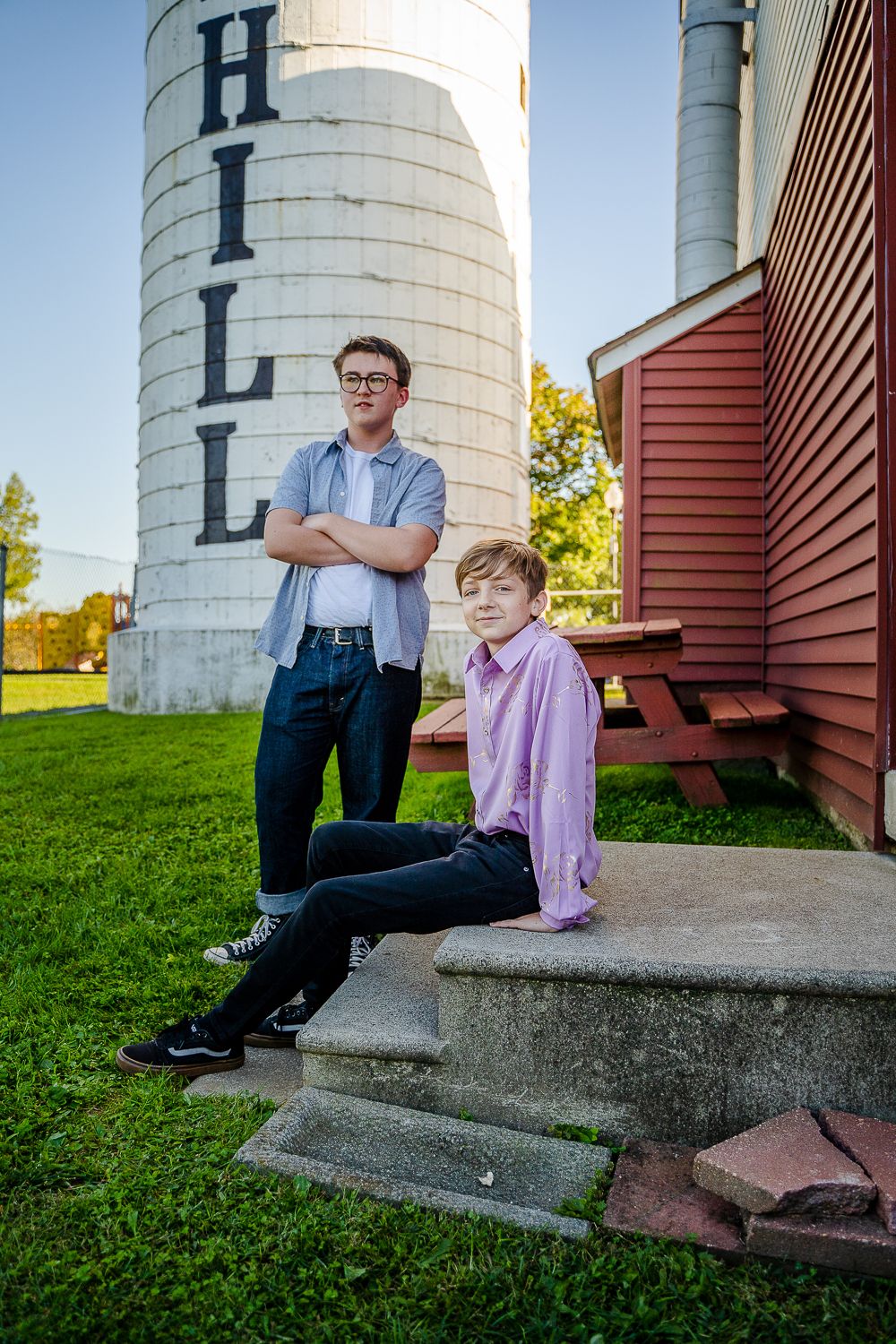 Two boys posing near a farm silo, one standing and one sitting on steps.