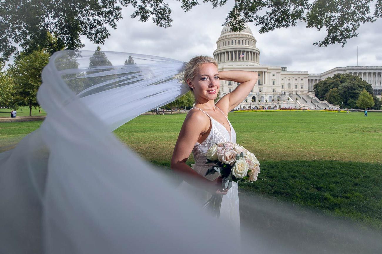 Bride in white gown with veil blowing in the wind holding bouquet at the US Capitol.