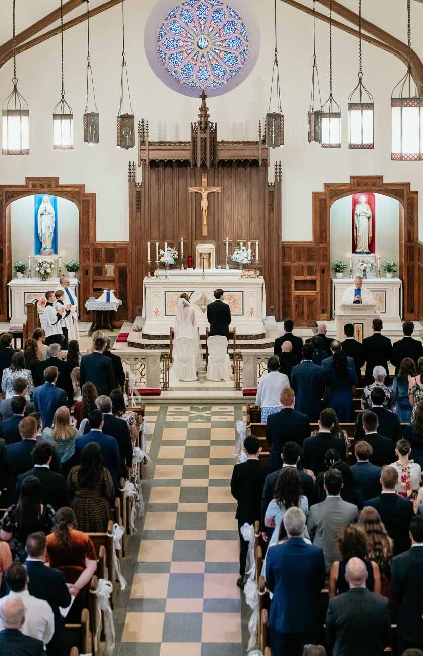 Catholic church wedding ceremony with couple at altar, rose window, and full congregation in attendance.