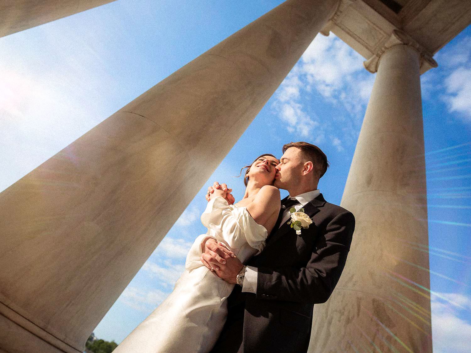 Low-angle shot of bride and groom embracing beneath grand marble columns at the Jefferson Memorial, Washington DC.