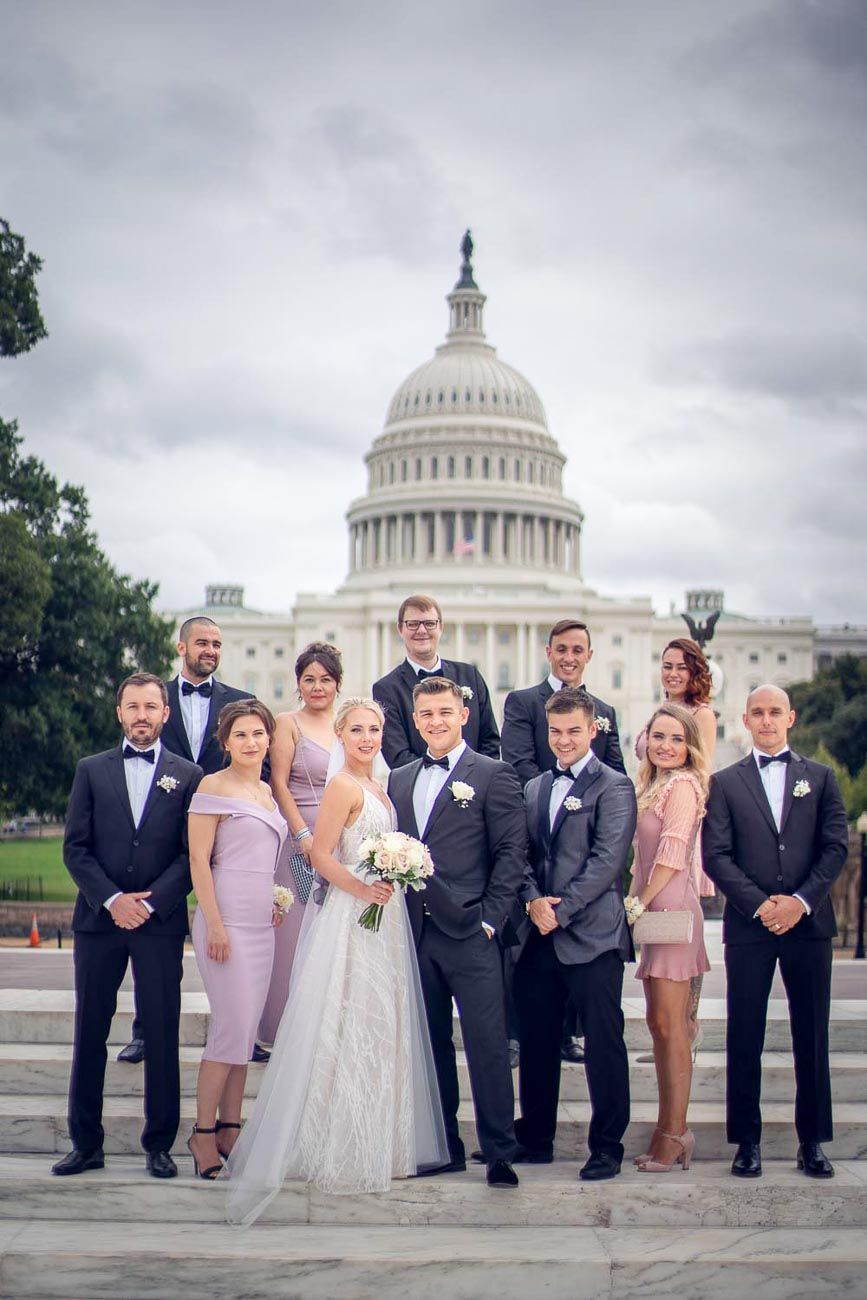 Full wedding party with bride, groom, groomsmen, and bridesmaids posing before the US Capitol building.