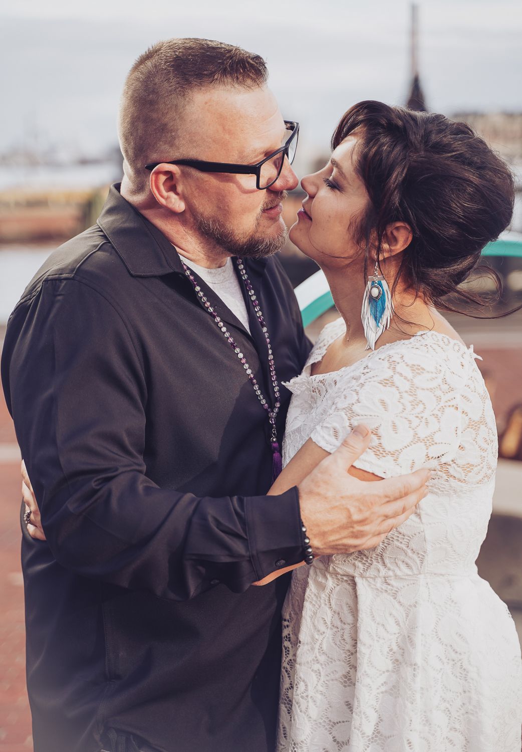 Newlywed couple sharing romantic kiss outdoors near harbor, bride in white lace dress.