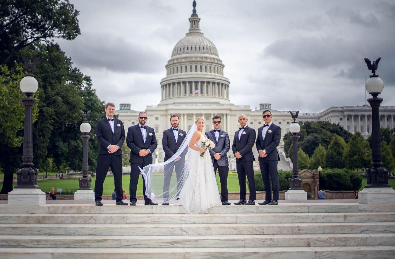 Bride and groomsmen pose on steps in front of the US Capitol building on a cloudy day.