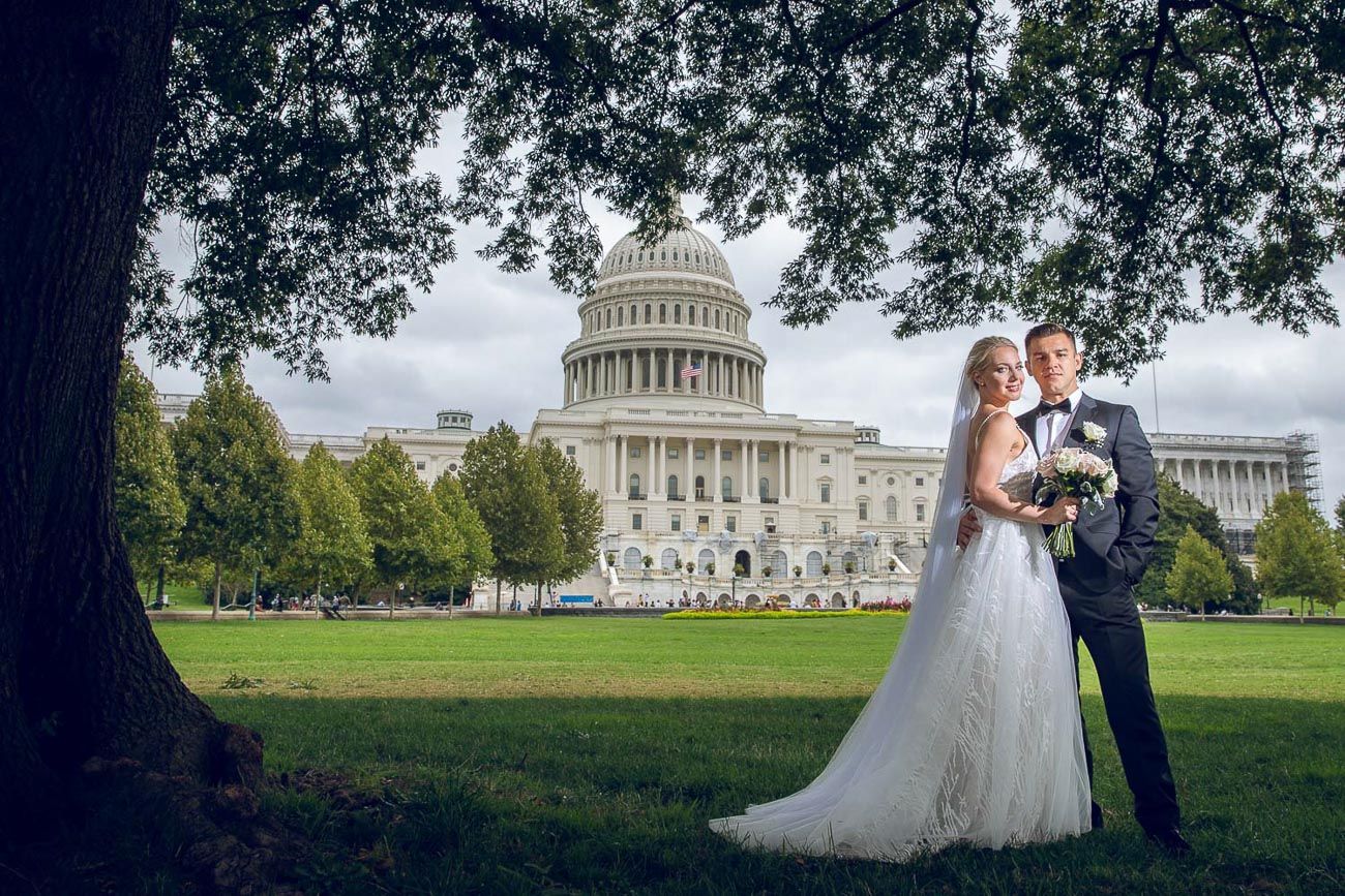 Bride and groom standing near a large tree with the US Capitol building behind them.