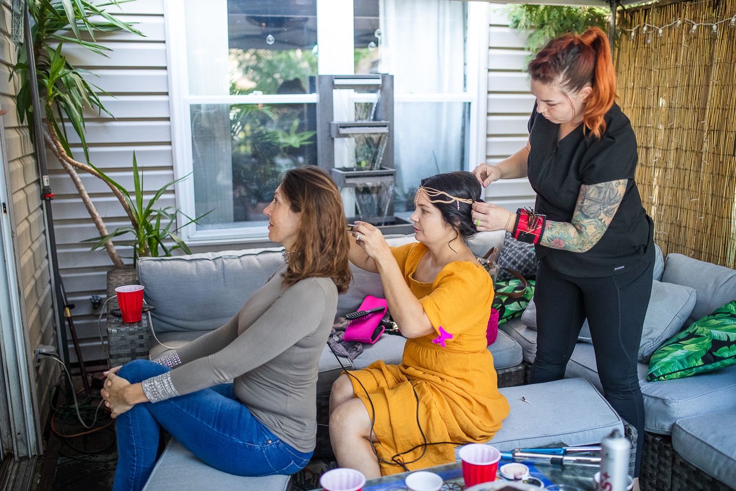 Bridal party getting hair and makeup done outdoors on a patio, including headpiece styling.