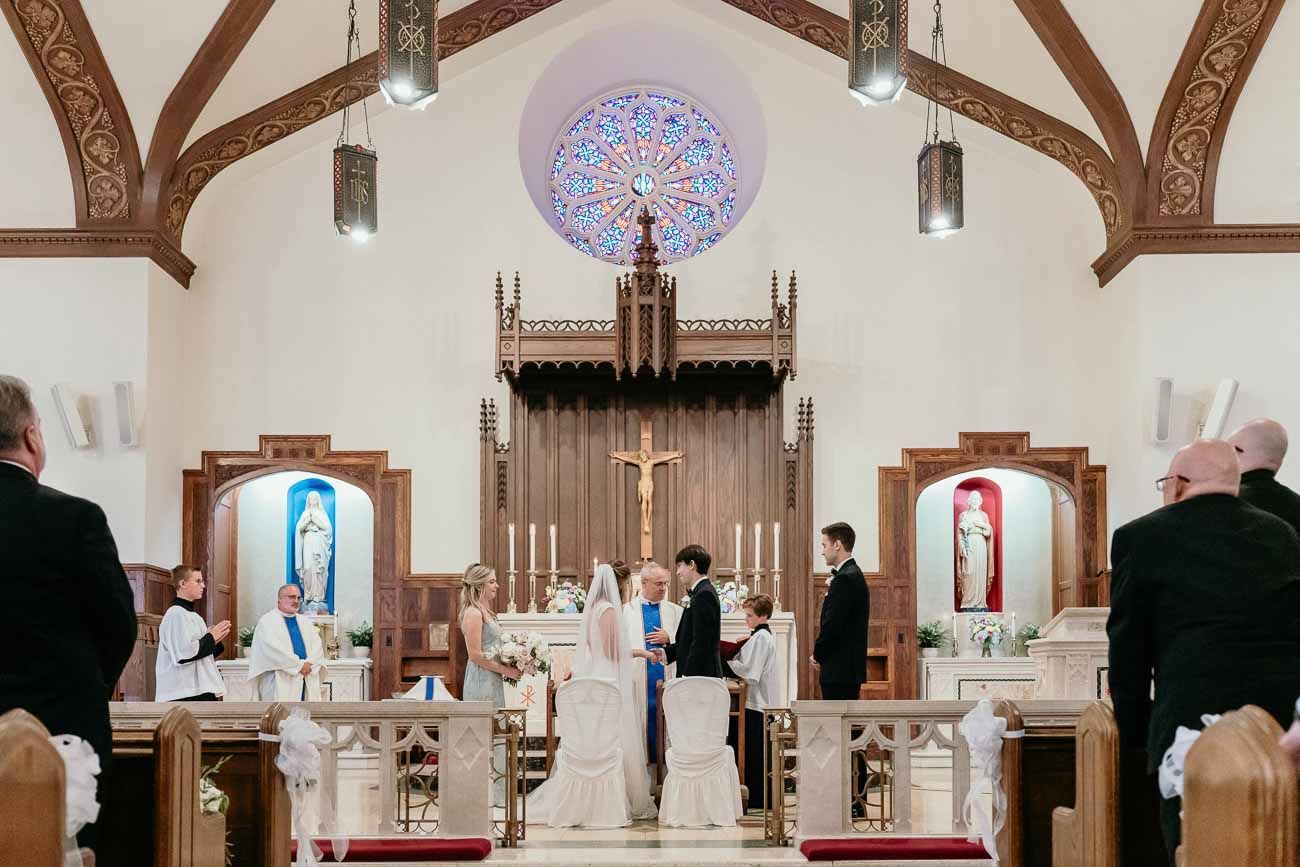 Wide shot of a Catholic church wedding ceremony at the altar with a rose window and crucifix.
