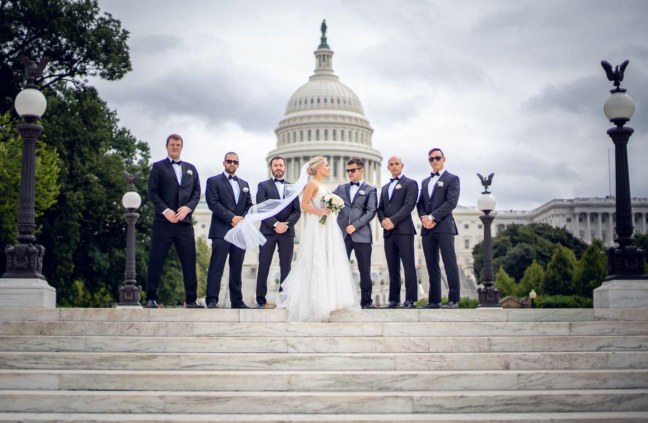 Bride and groom with groomsmen on Capitol Building steps on cloudy wedding day.