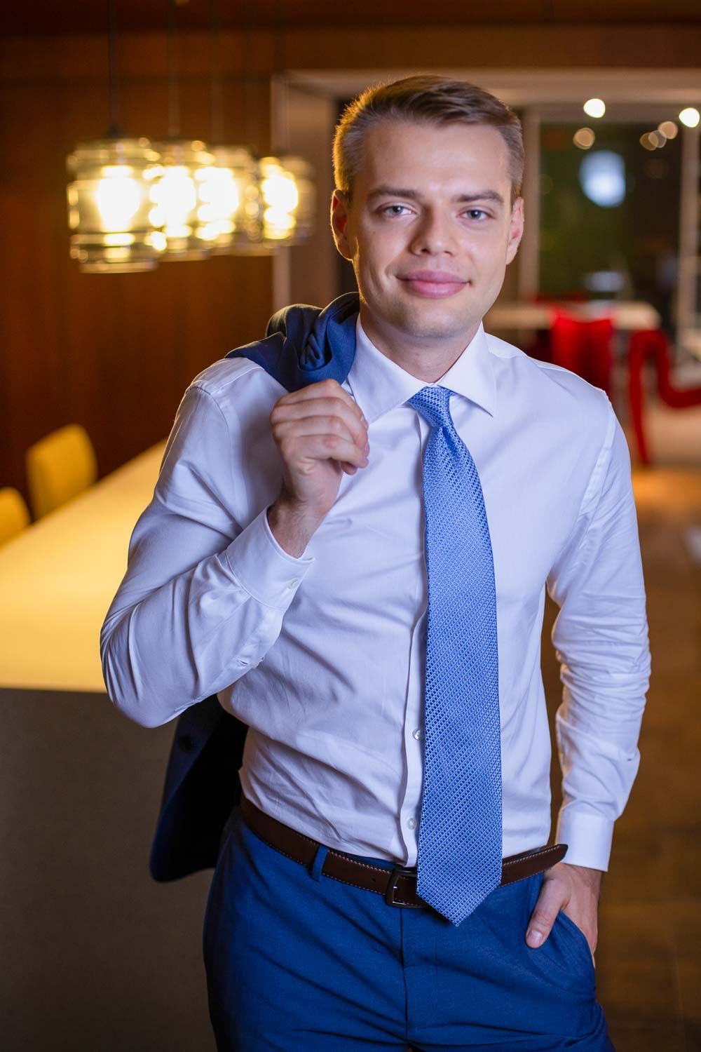 Confident young man in a blue suit and tie holding his jacket over his shoulder in an elegant venue.