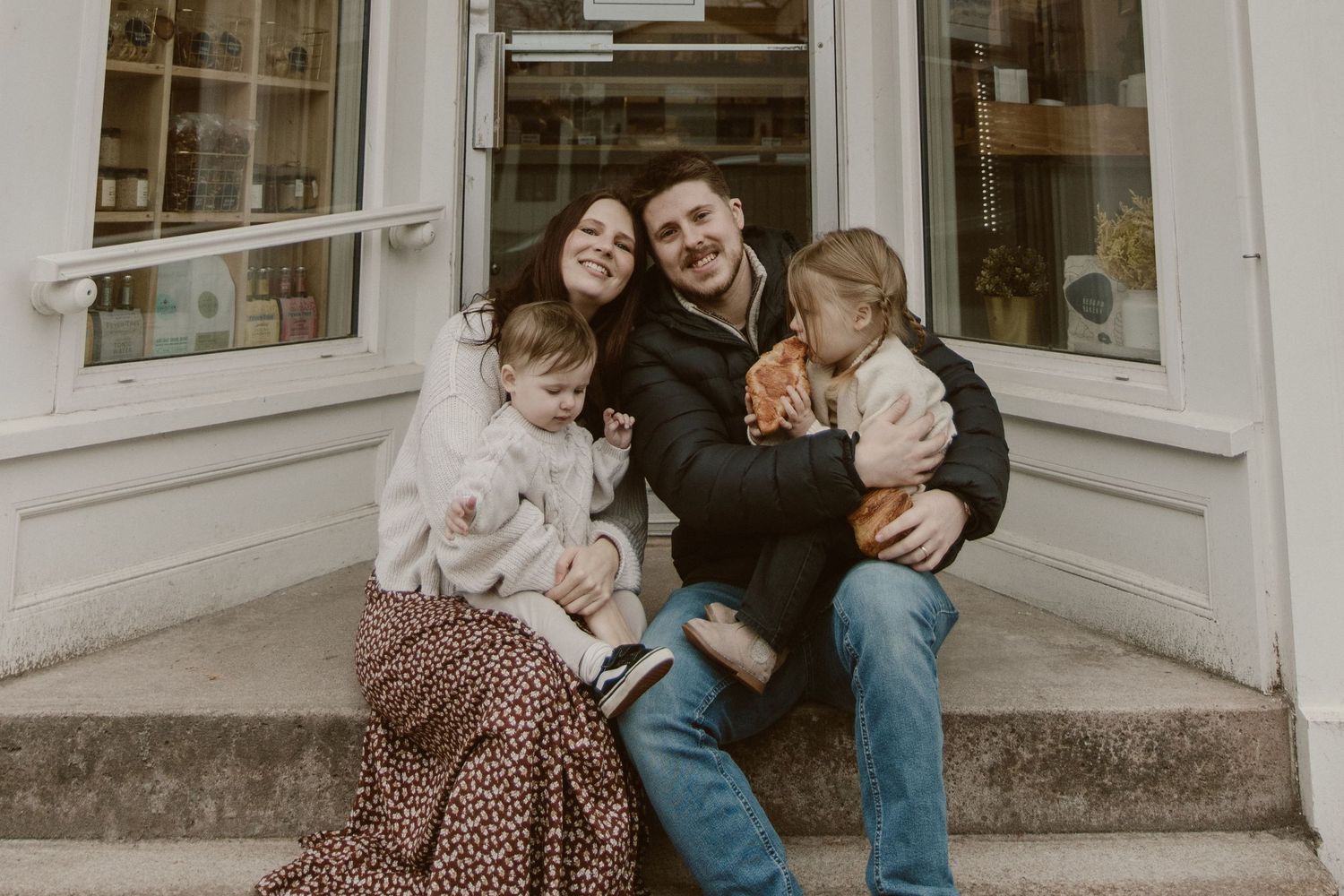 Family sitting together on storefront steps sharing a warm moment.