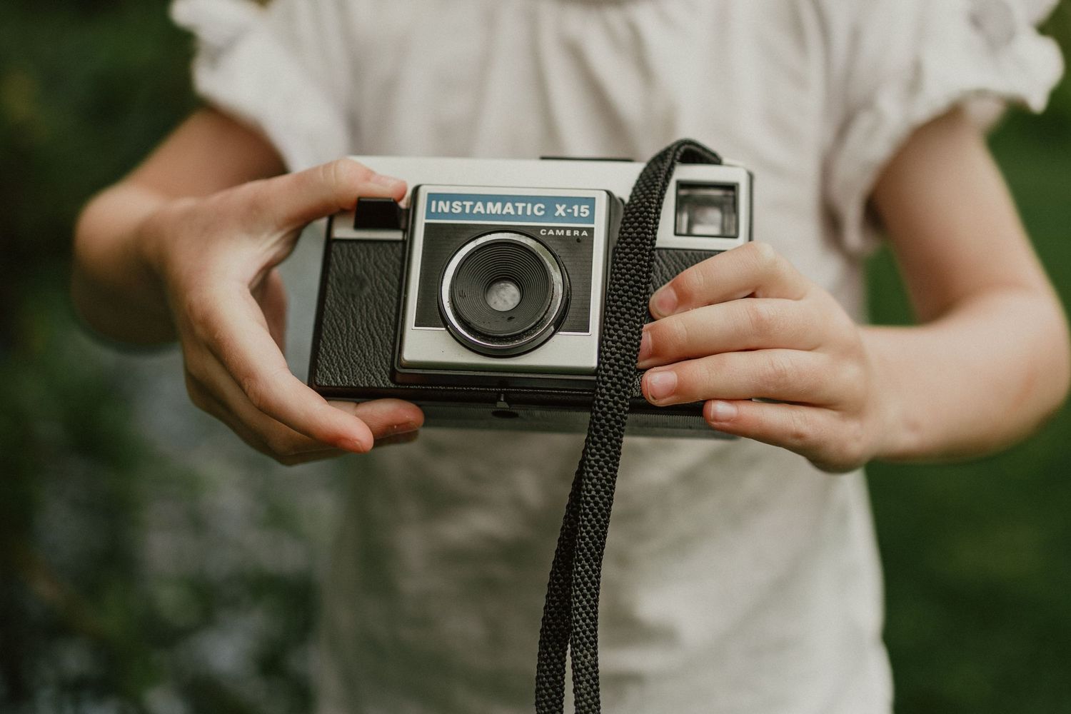 Hands holding vintage Instamatic camera against white blouse background.