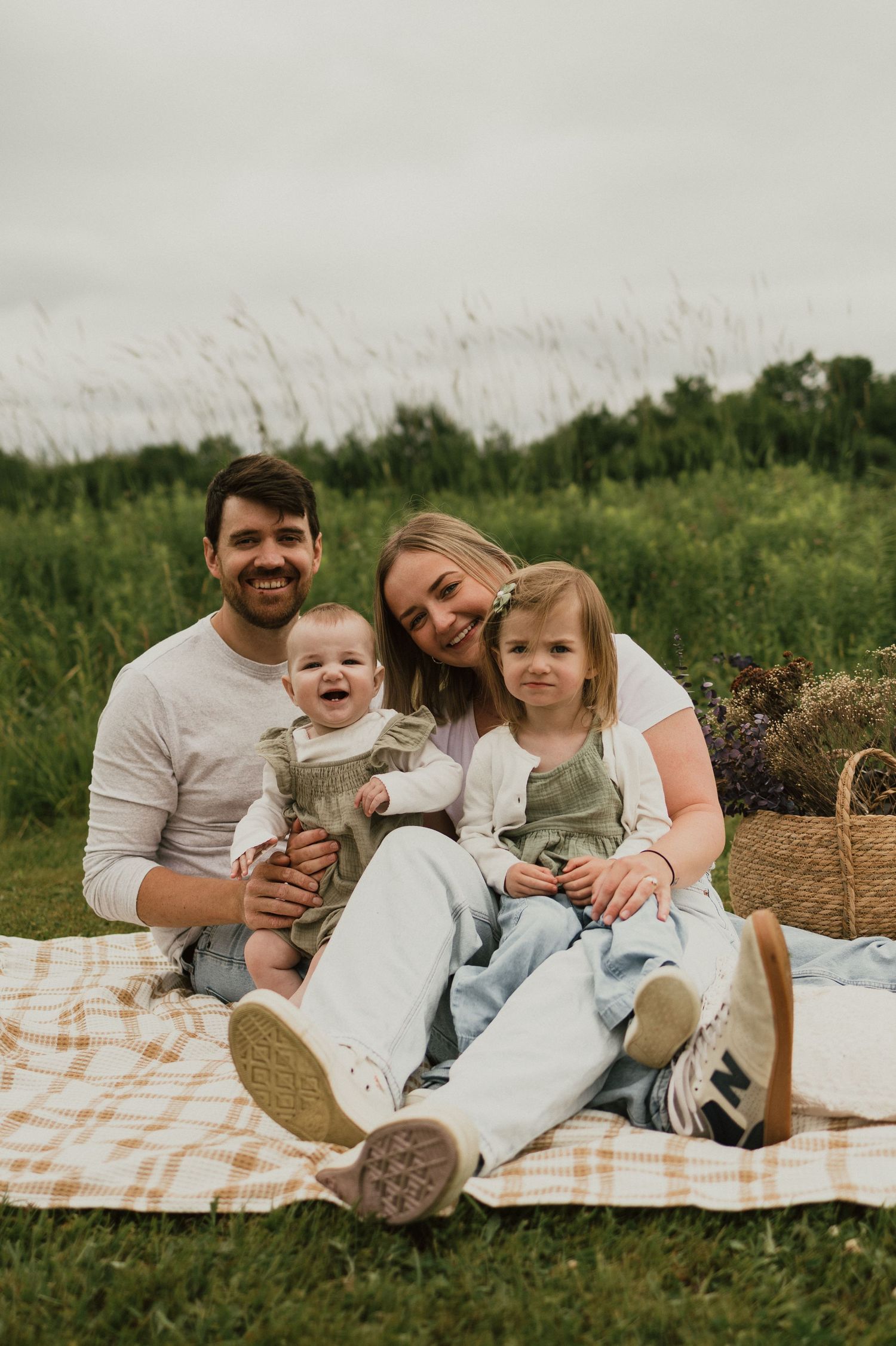 A family sits together on a checkered blanket for a picnic in a grassy field on a sunny day.