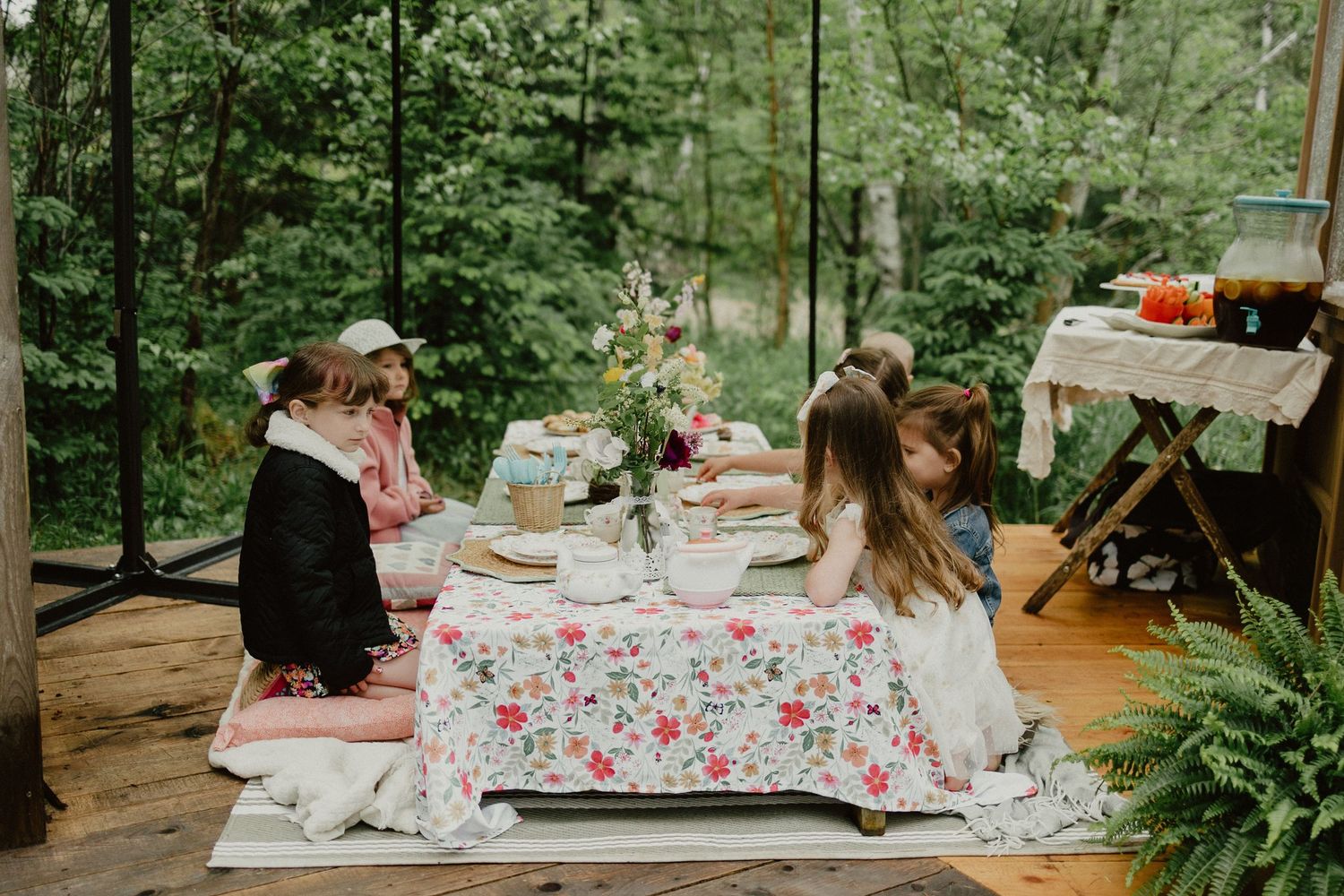 Rustic outdoor wedding reception tables set with floral tablecloths and greenery decor in a forest setting.