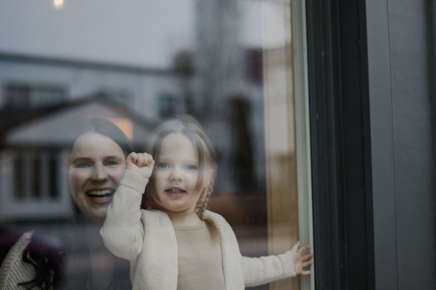 Two figures seen through window glass with joyful expressions.