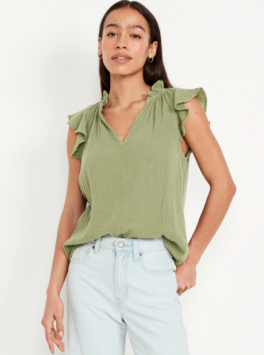 Sage green sleeveless blouse with ruffle details and v-neckline paired with light wash jeans.