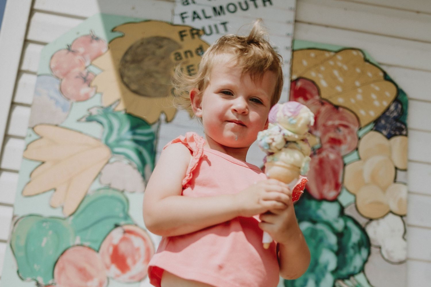 Young person holding ice cream cone in front of colorful painted wall mural.