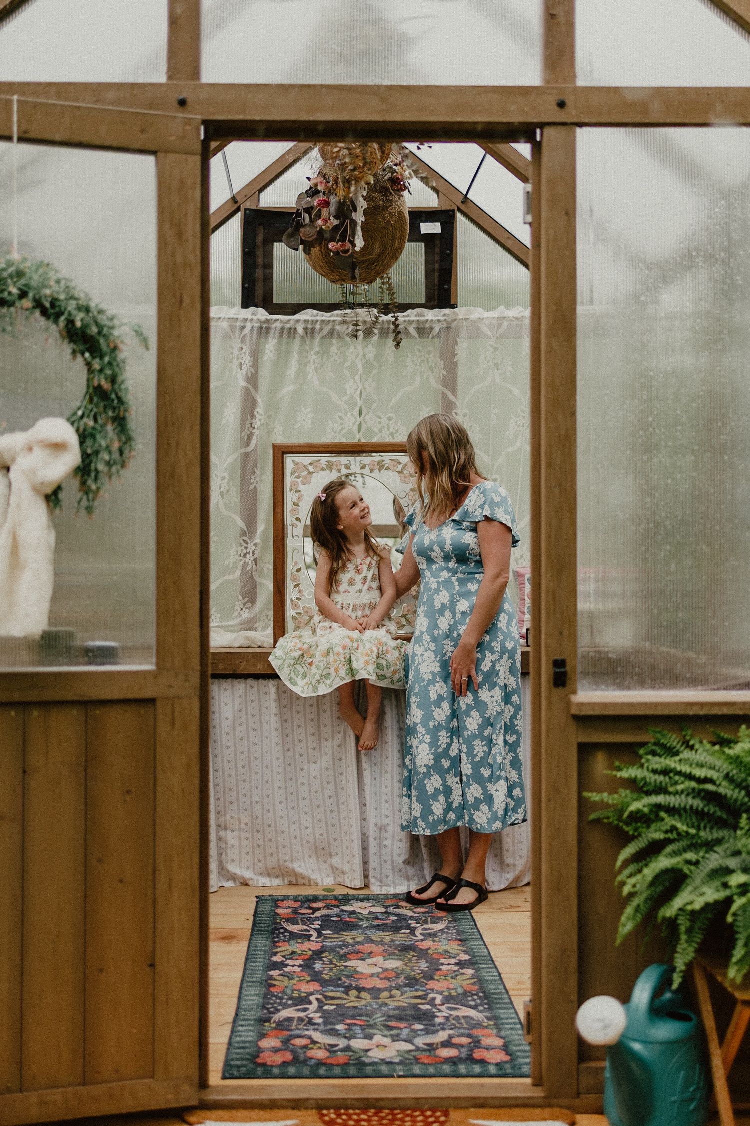 Three connected photos show someone in a blue floral dress dancing and joyfully twirling on a patterned rug inside a wooden greenhouse.