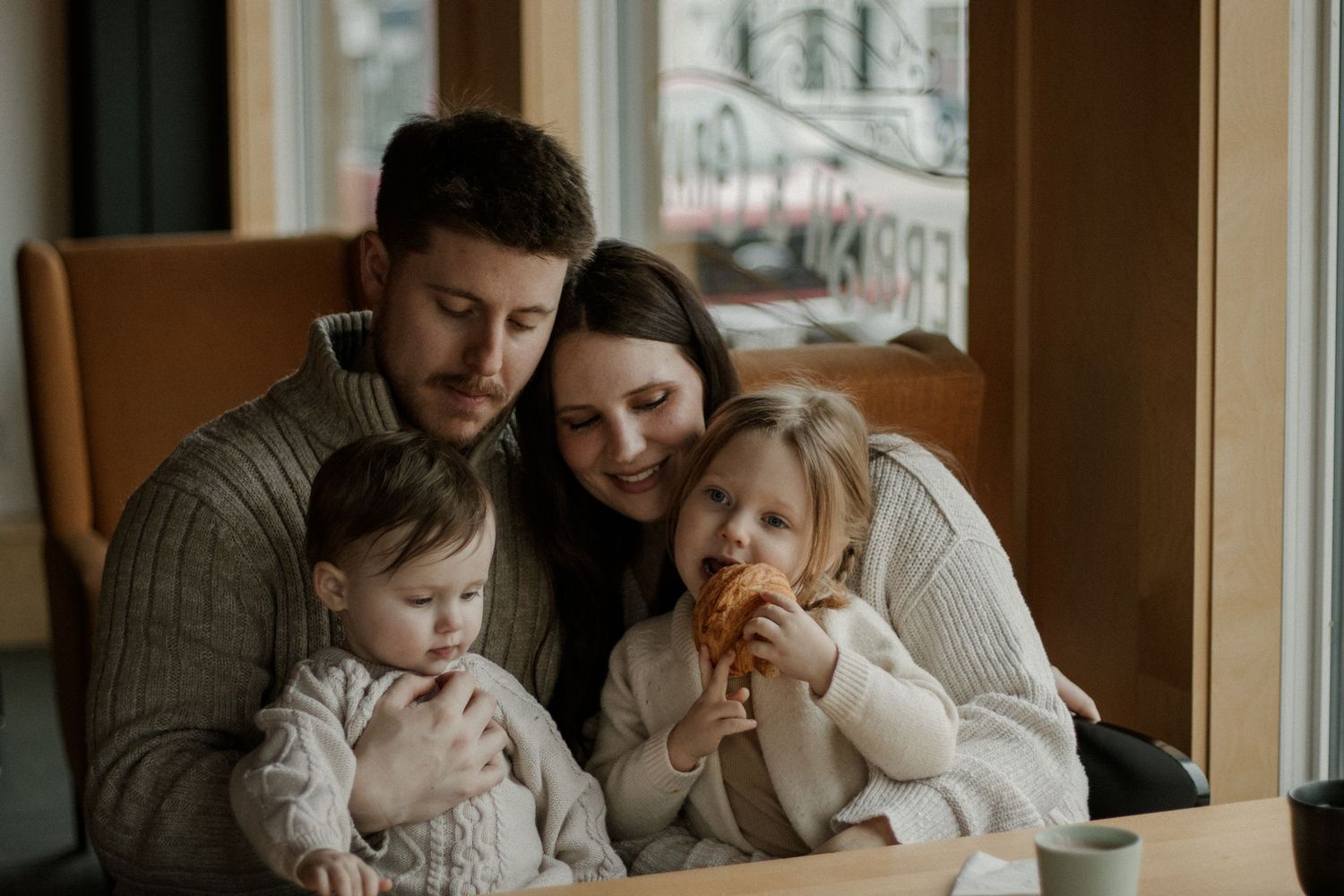 Family cuddling together on couch by window in cozy winter scene.