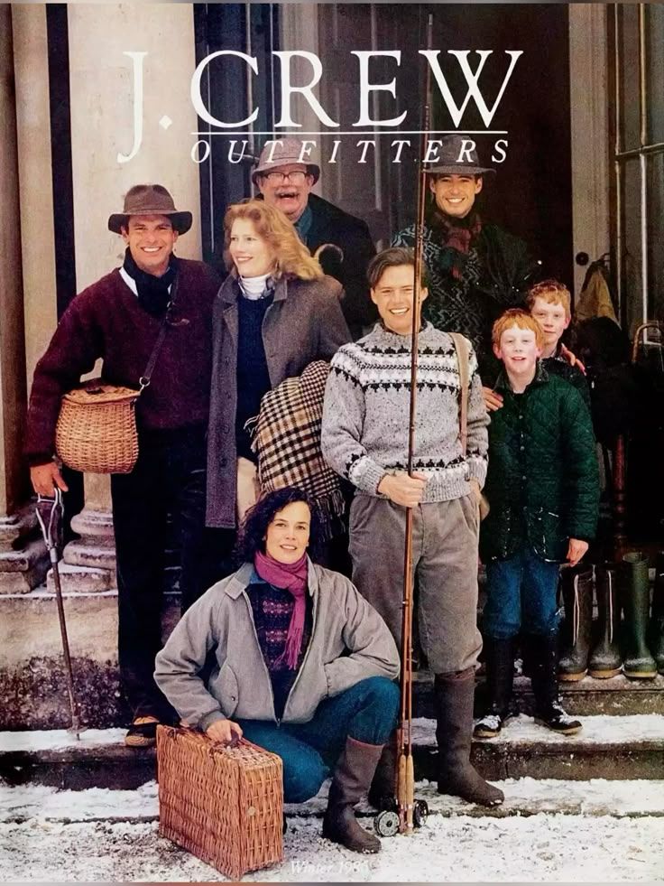 J.Crew fashion advertisement showing people in winter outerwear and knitwear posing outside store in snowy setting.