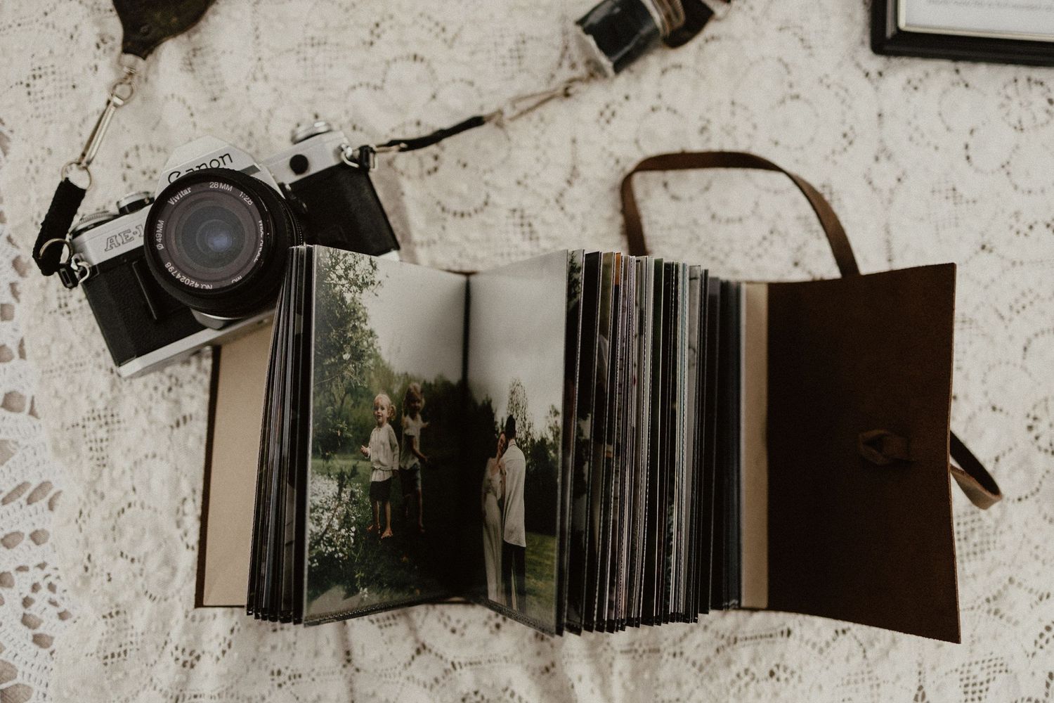 Vintage camera and leather photo album with printed photographs laid out on a textured white surface.