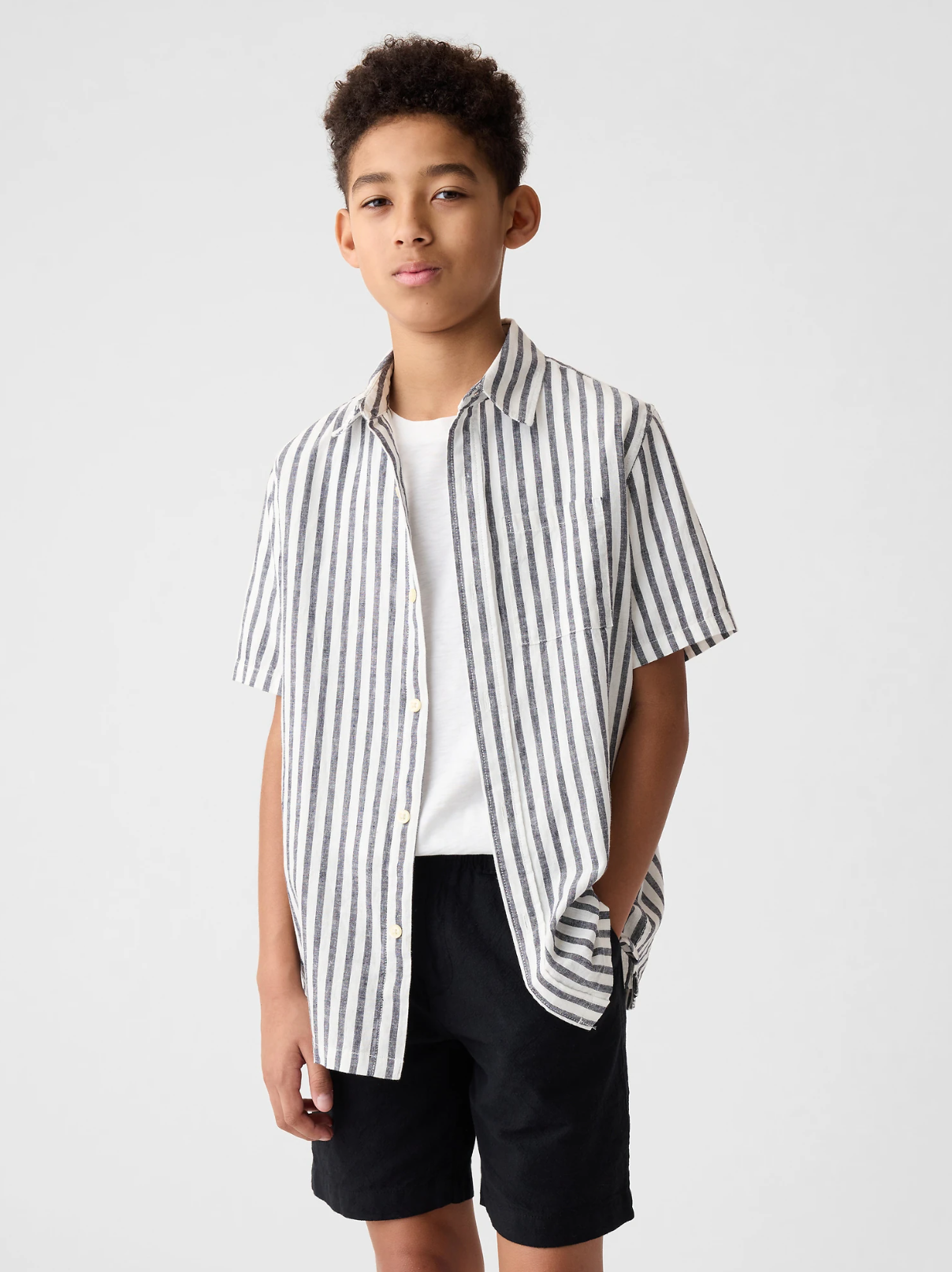 Young model wearing a casual striped short-sleeve button-up shirt with black shorts against white background.
