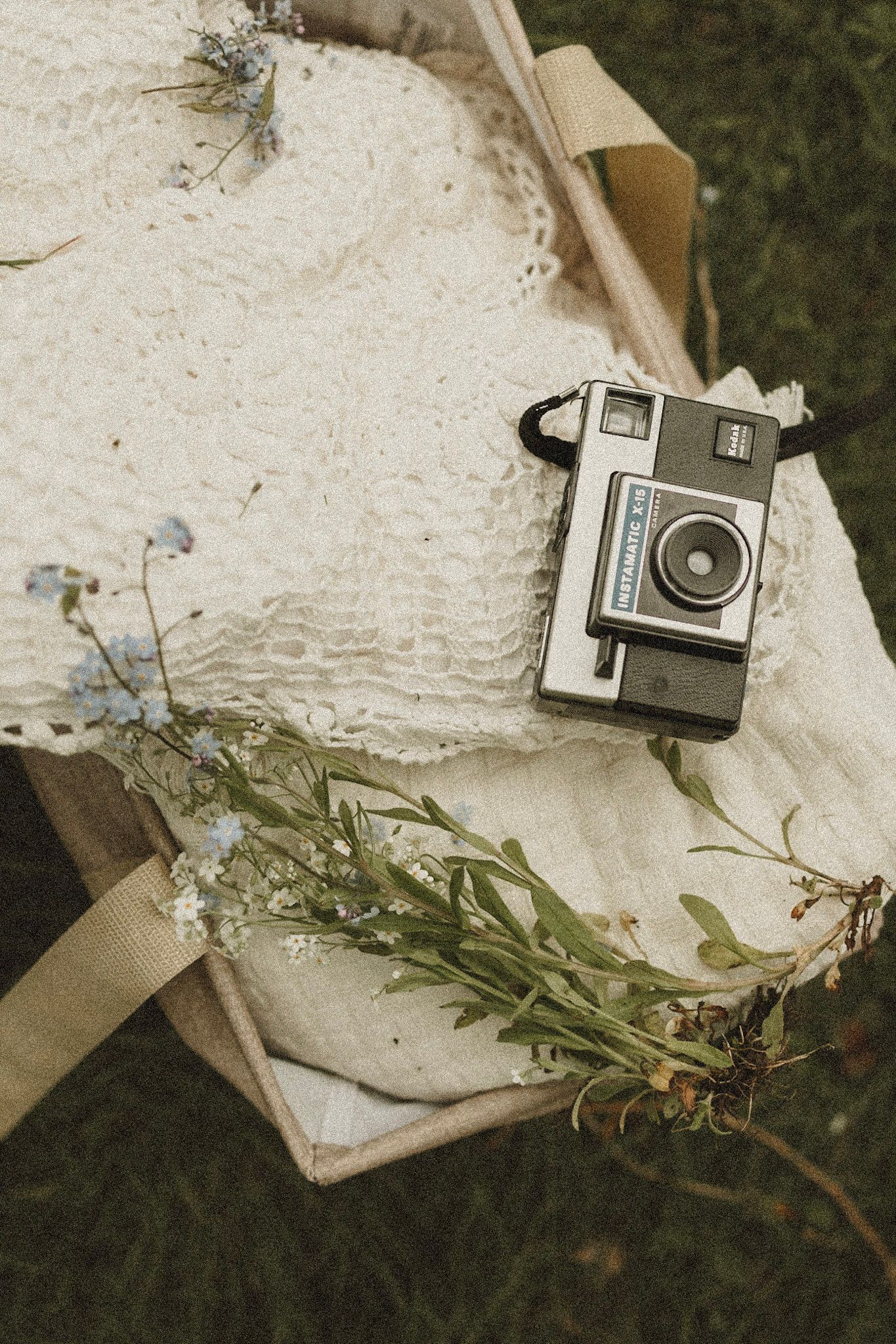 Vintage Polaroid camera rests on white fabric with delicate dried flowers creating a nostalgic flat lay composition.