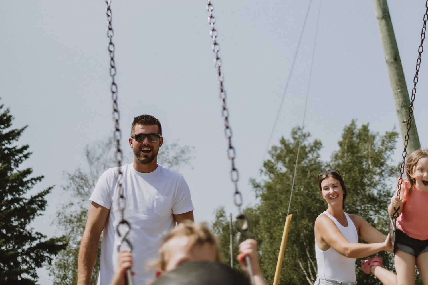 People enjoying quality family time together on playground swings in a park on a sunny day.