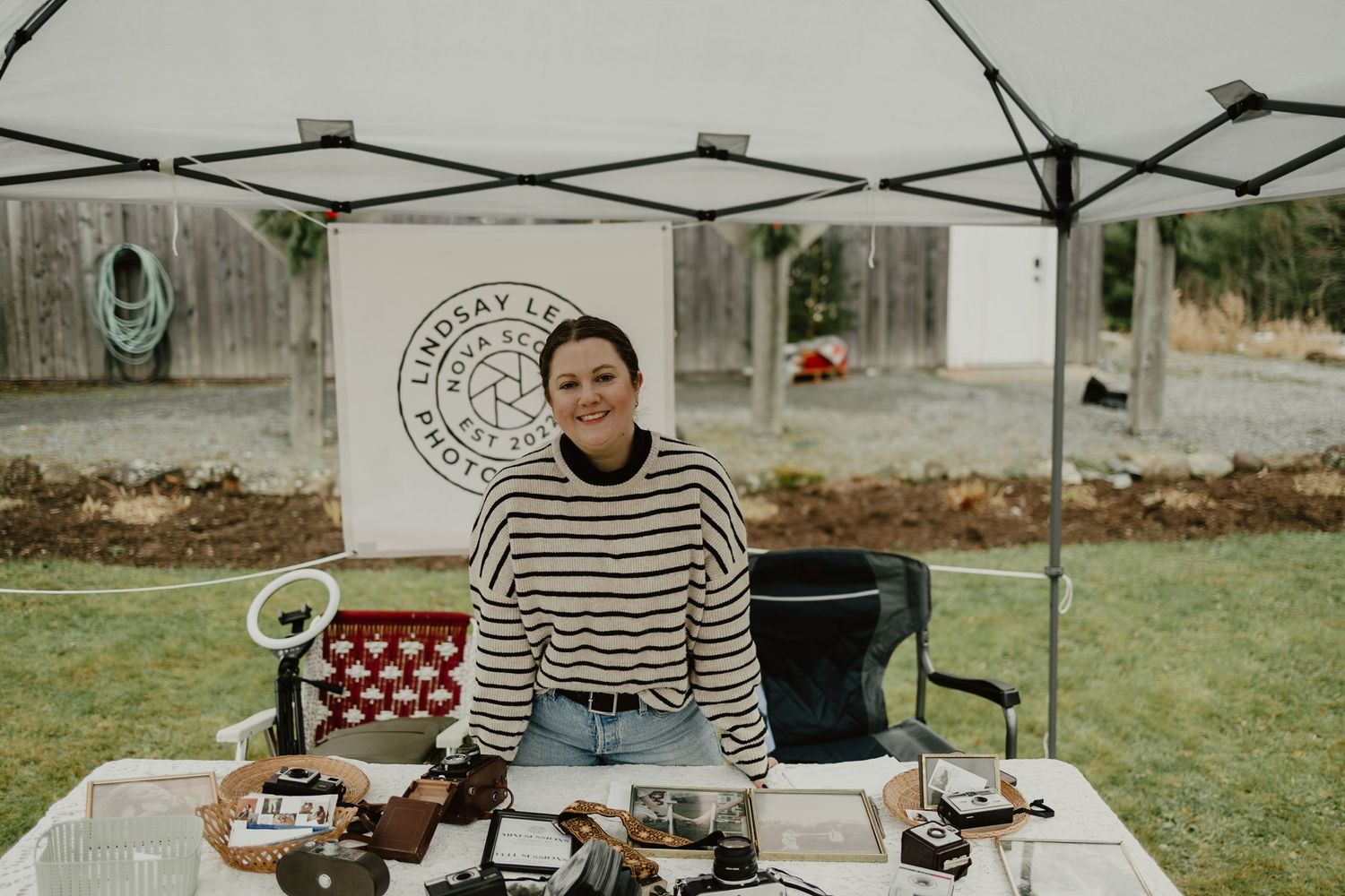 Vintage typewriter setup at outdoor market booth with striped sweater seller and red chair under white tent canopy.