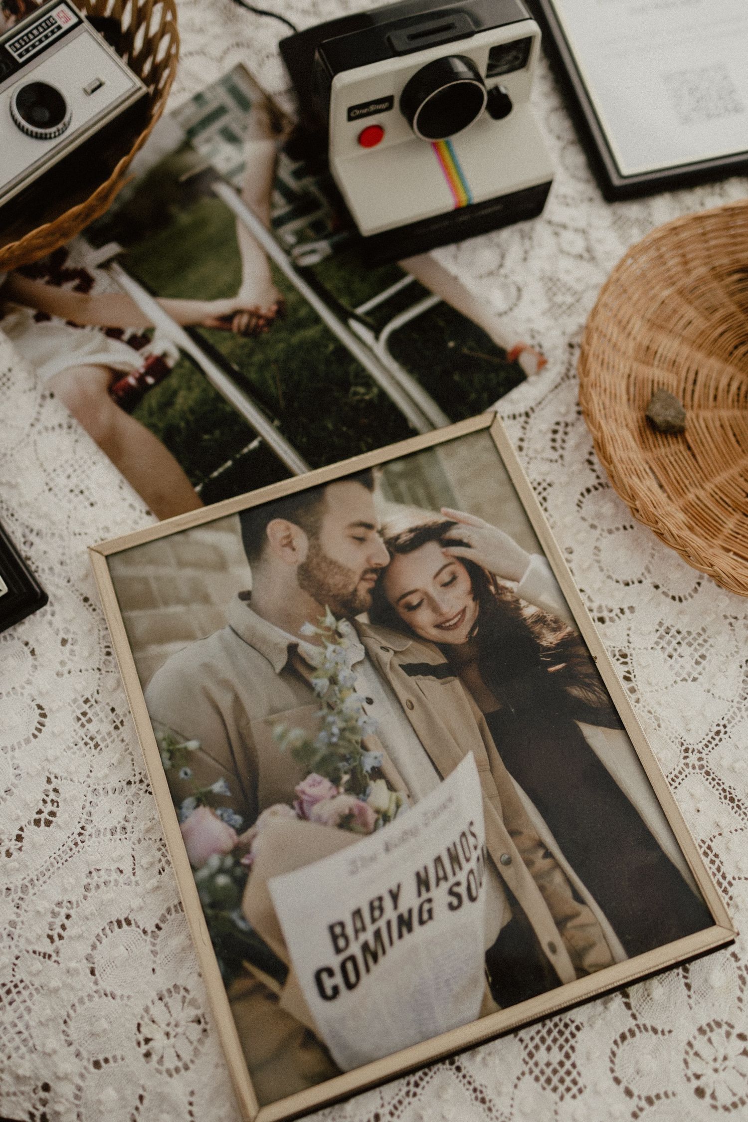 Vintage Polaroid cameras and photographs arranged on white lace tablecloth with nostalgic sepia toned prints.