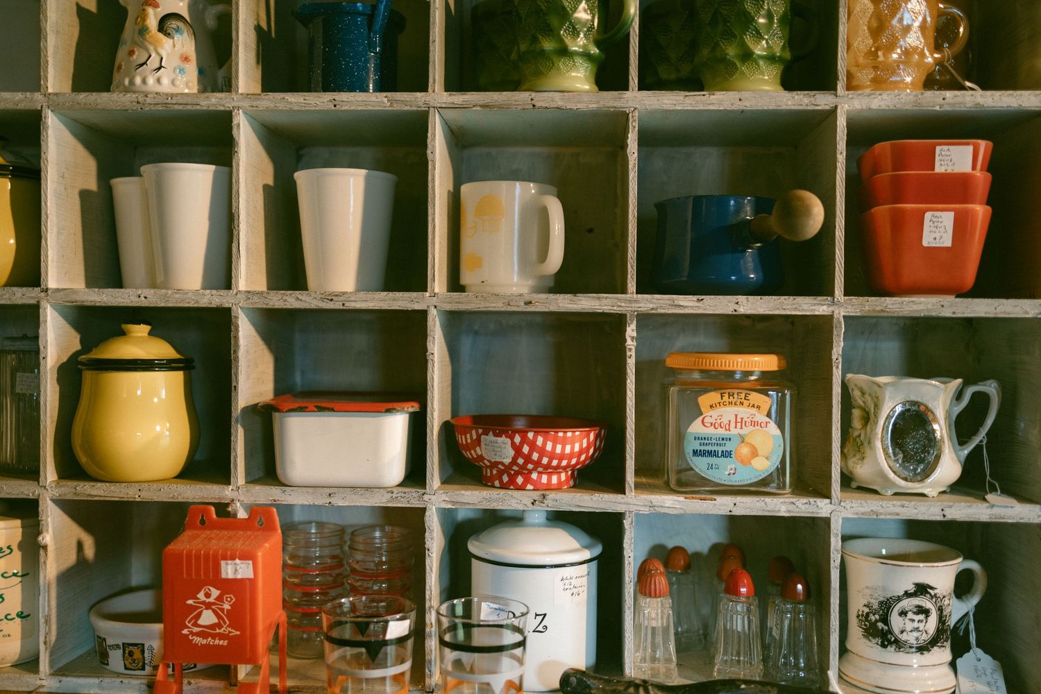 Collection of vintage mugs, jars, and containers displayed on wooden cubby shelf storage unit in rustic retro style.