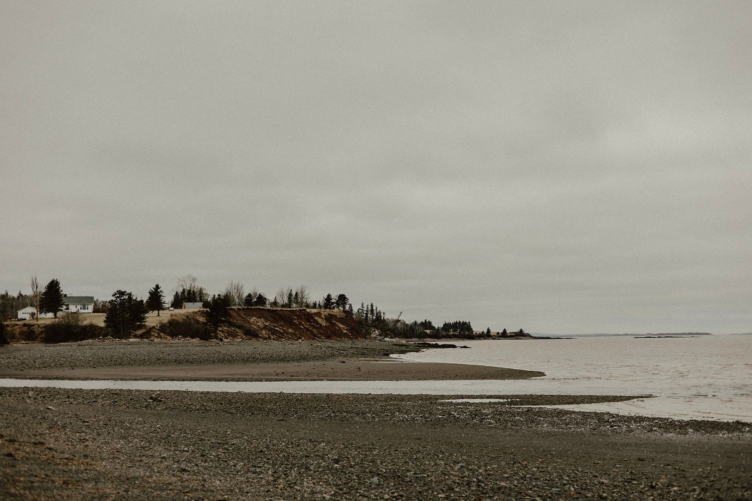 A coastal town sits on cliffs overlooking a rocky beach under grey skies.