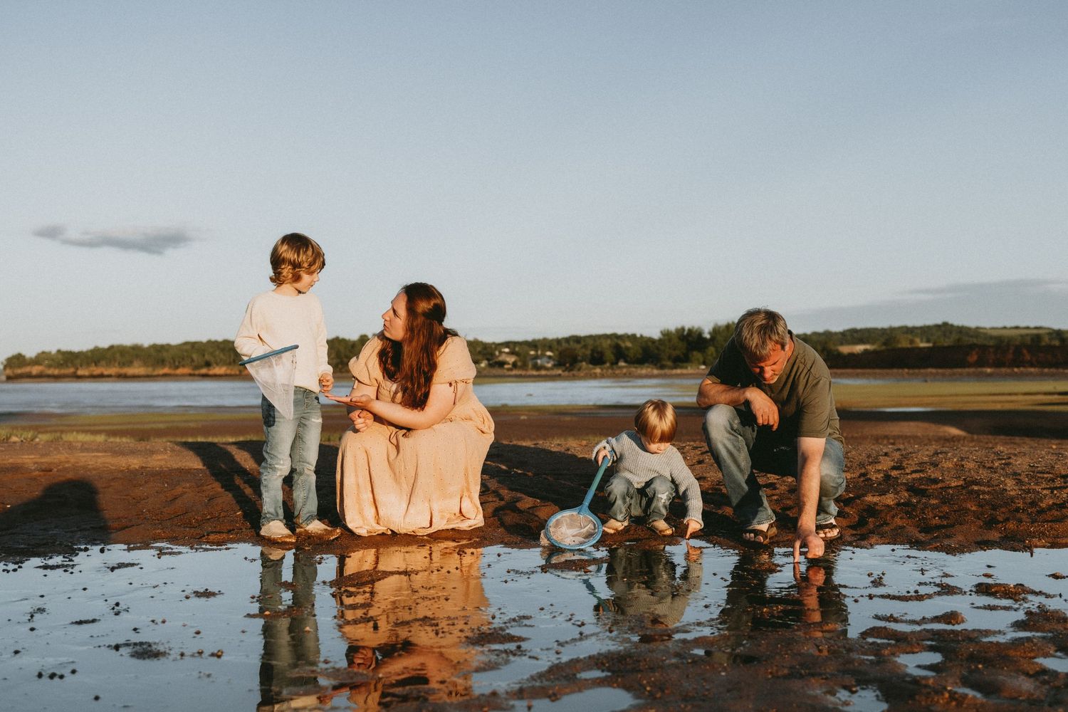 Family playing and splashing in shallow coastal waters during golden hour.