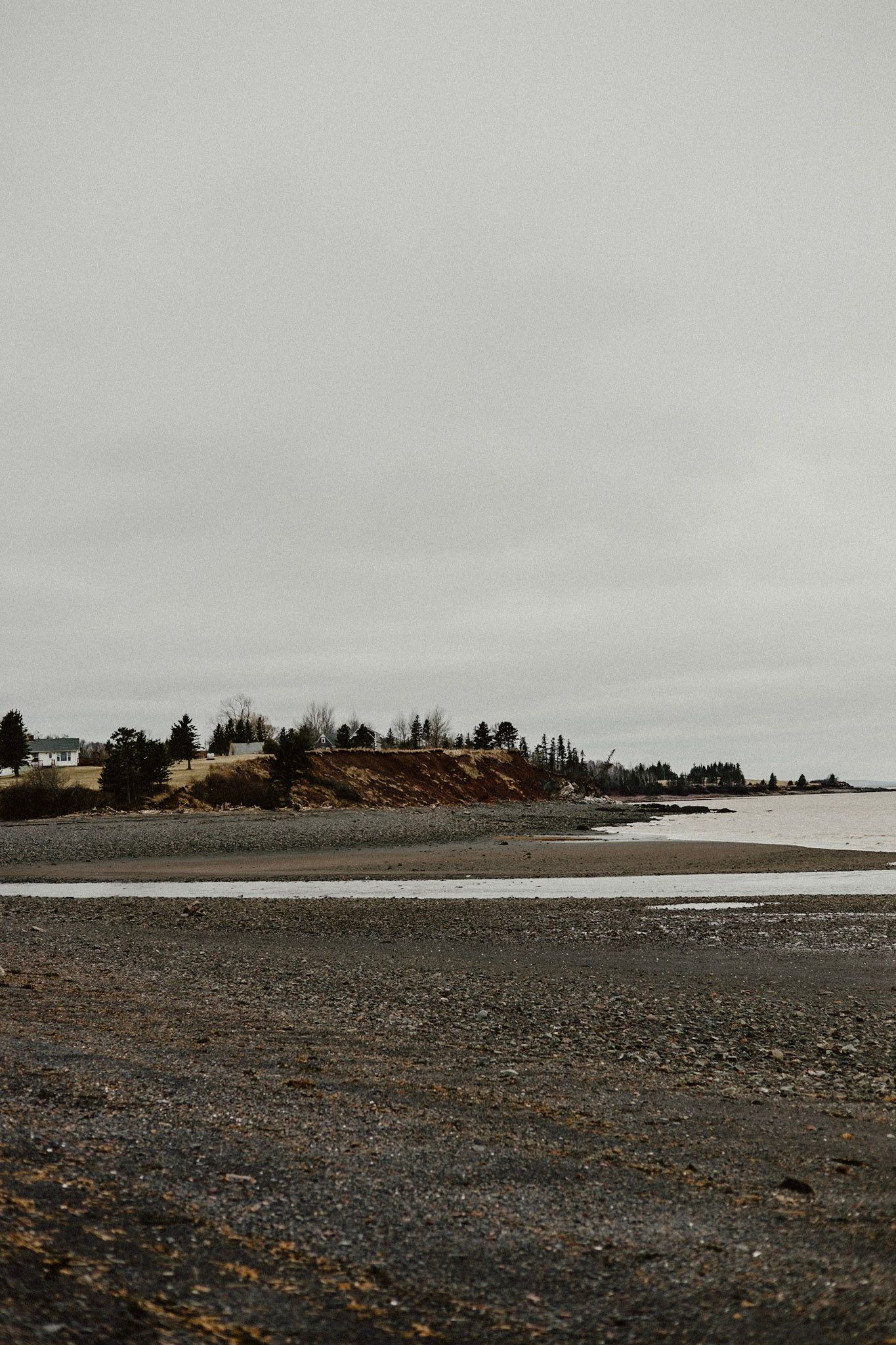 Rocky coastline with houses perched on cliffs above a grey beach.