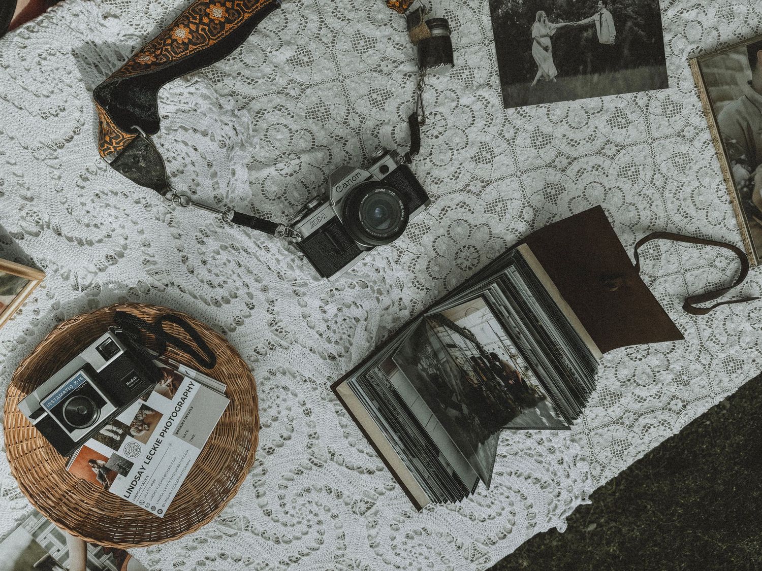 Vintage photography equipment and black and white photos displayed on a textured lace tablecloth.