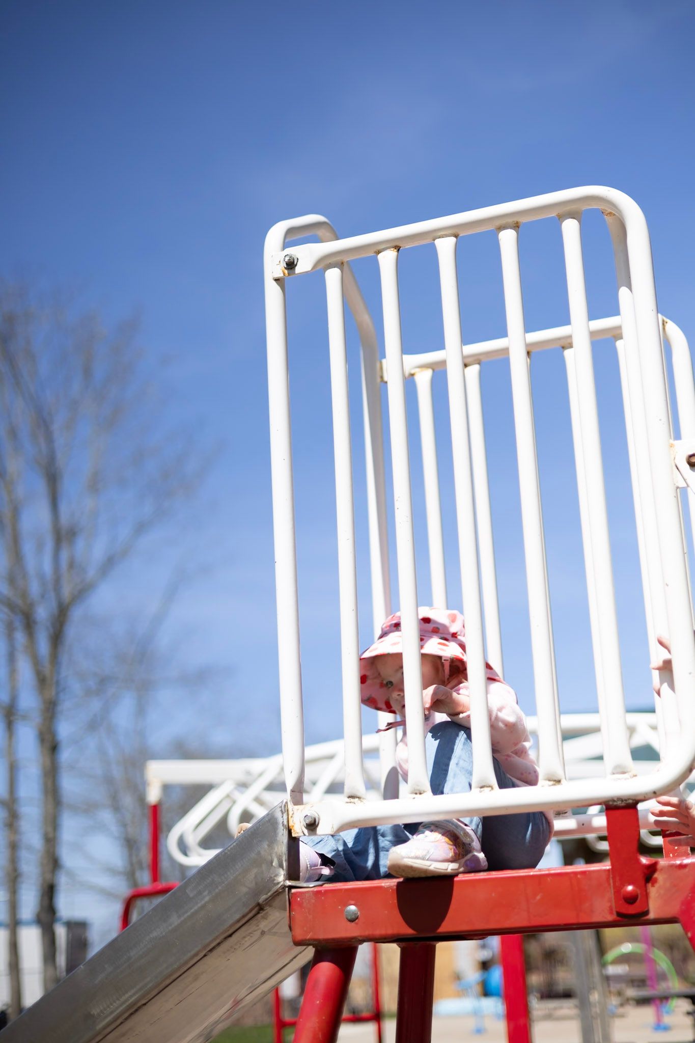 Child playing on red playground equipment with white safety railing against blue sky.