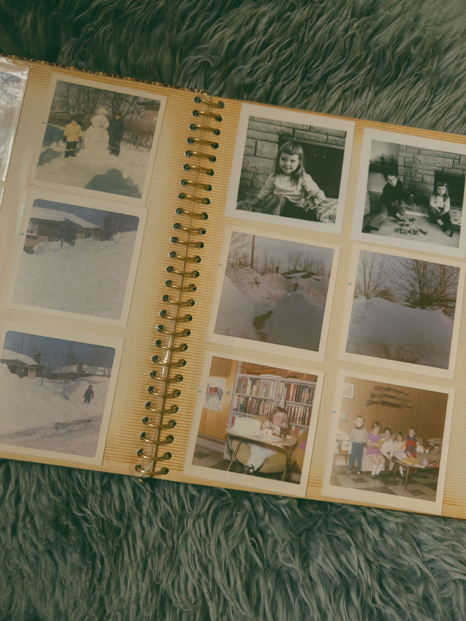 A vintage spiral-bound photo album displays black and white snapshots of winter scenes and family moments on its open pages.