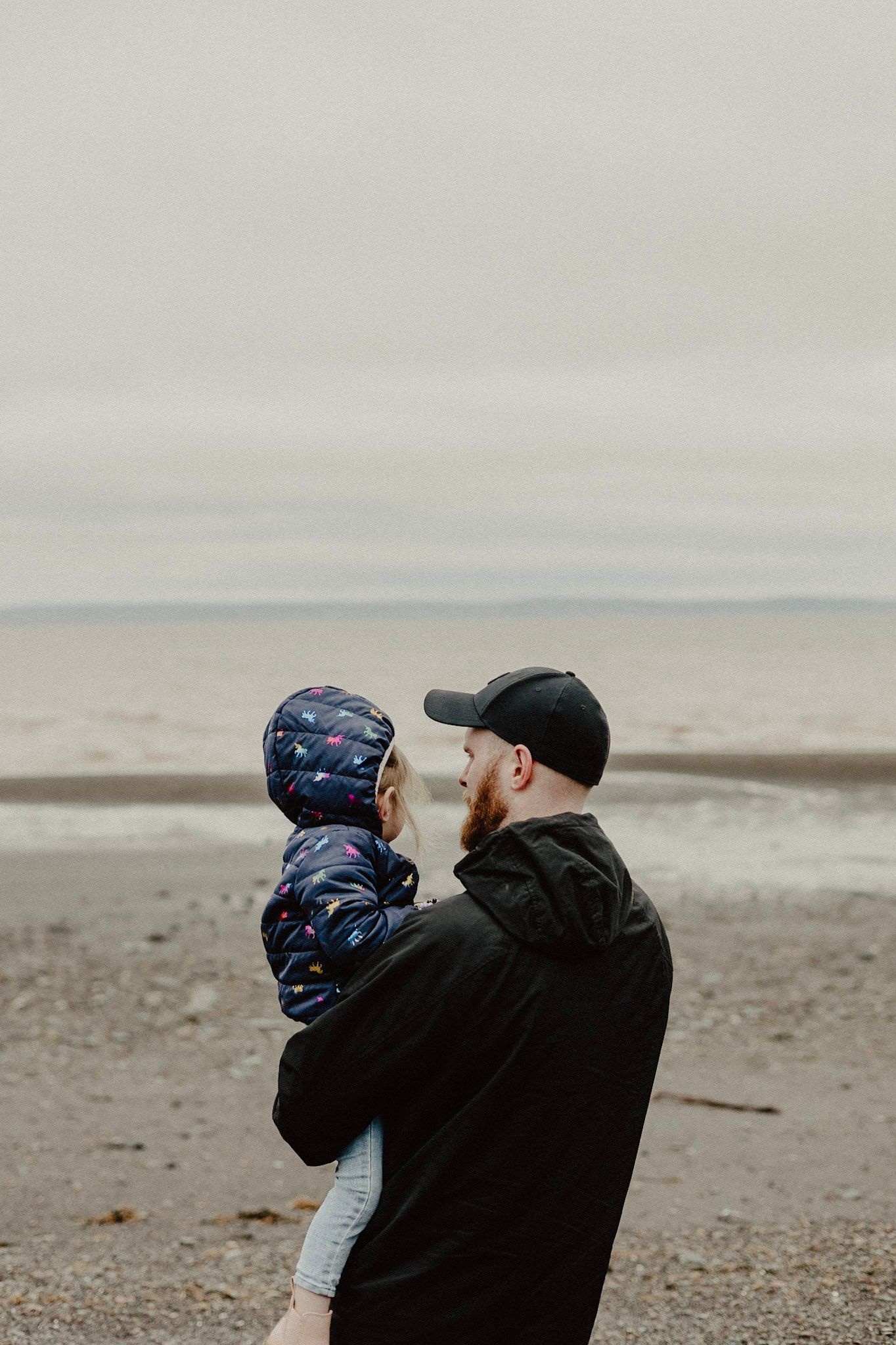 Two figures share an intimate moment on a deserted beach under cloudy skies.