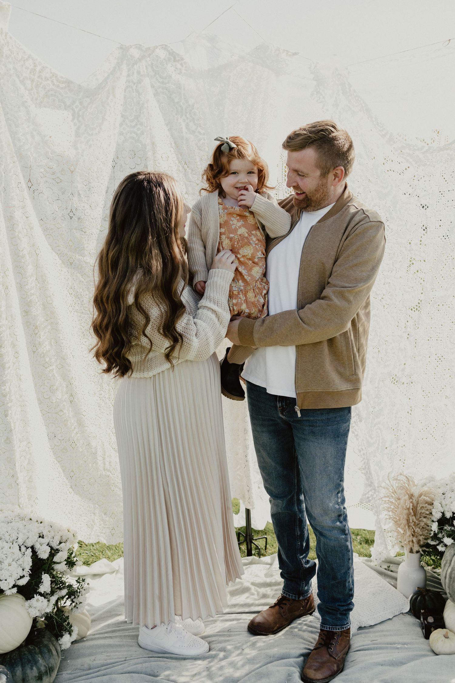 Family together in a warm embrace wearing neutral tones against a white backdrop with subtle mountain decor.