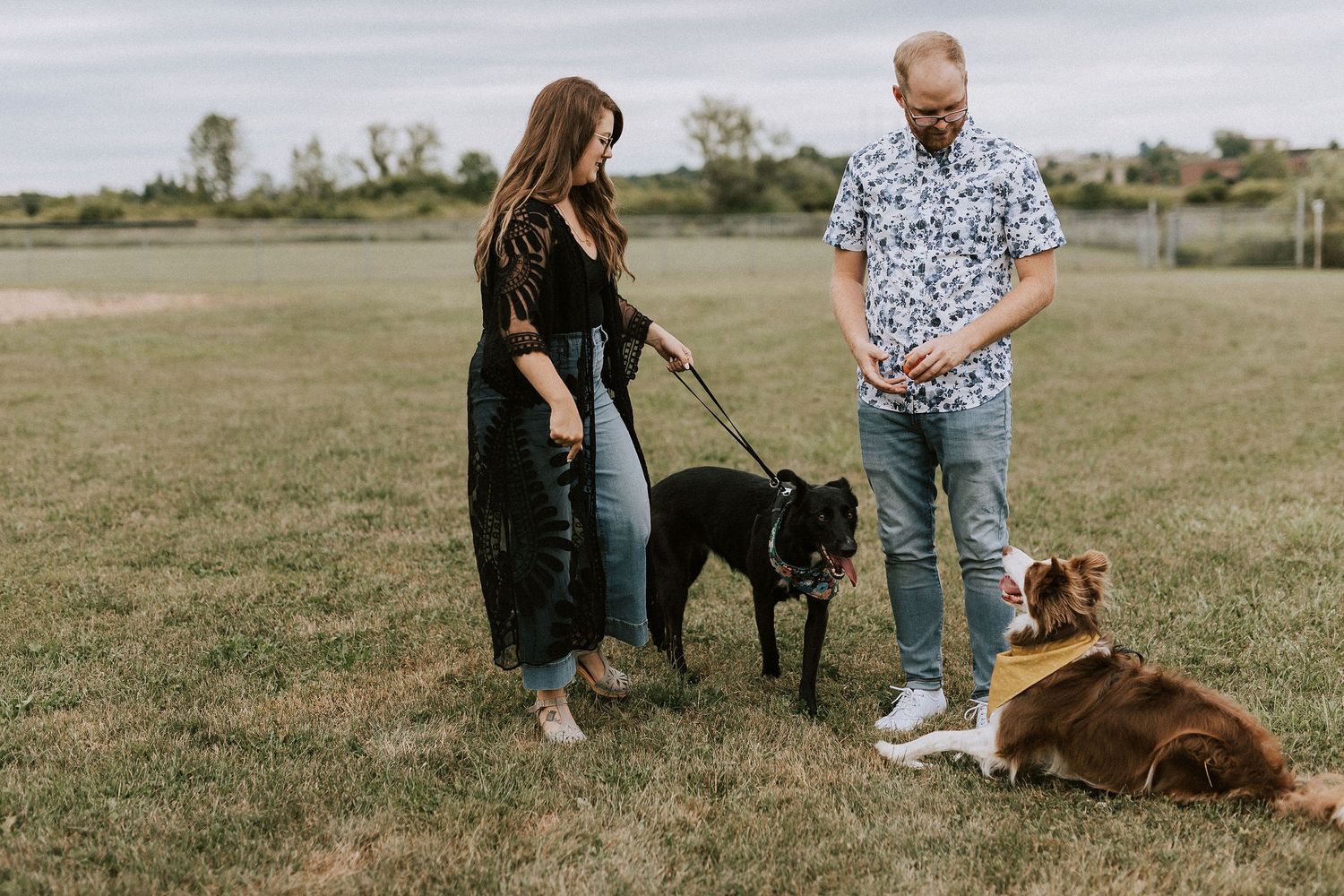 Couple with their dogs enjoying time together in an open field on a sunny day.