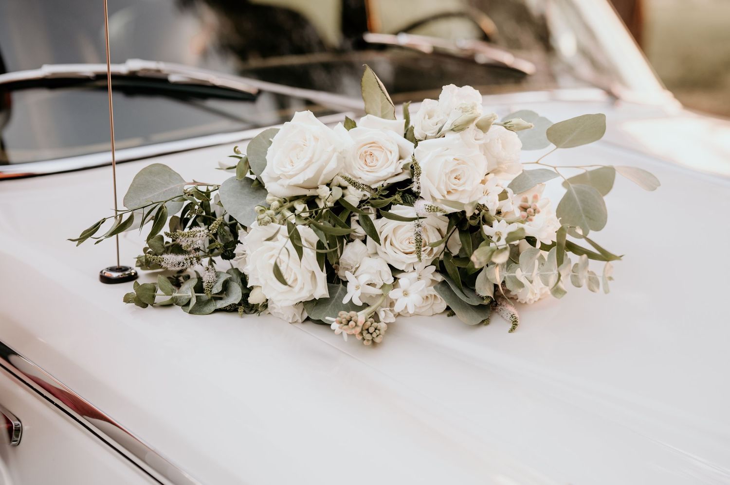 A white wedding flower bouquet sitting on a vintage car