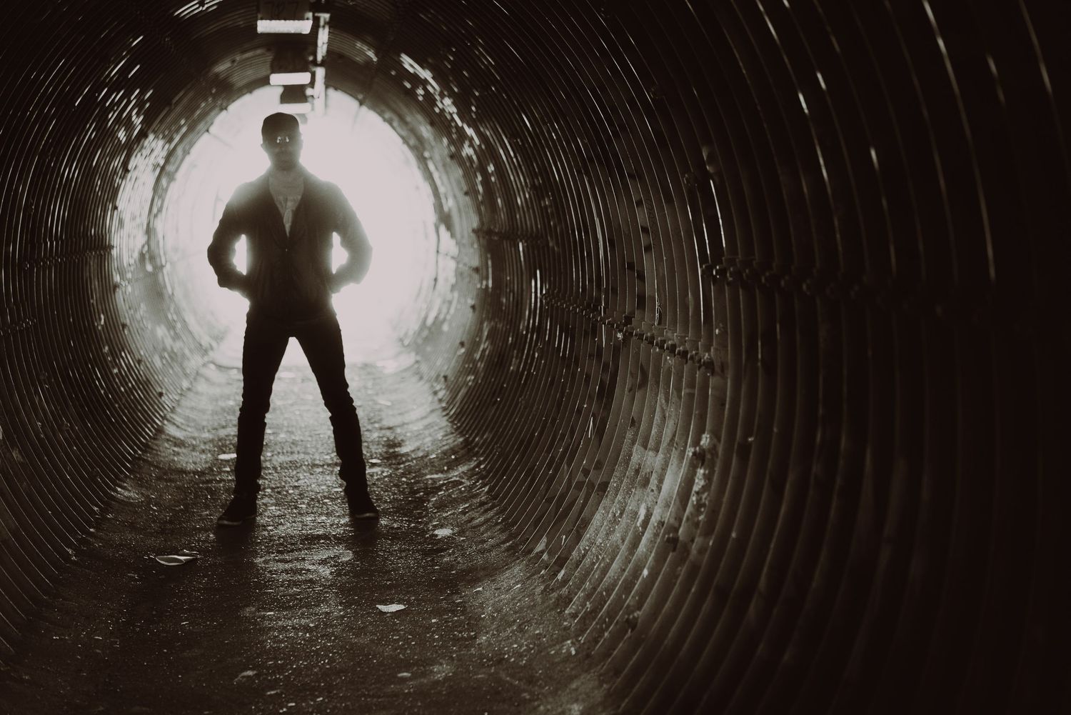Silhouette of a person with arms outstretched standing in a circular tunnel illuminated from behind, photographer Alec Watson