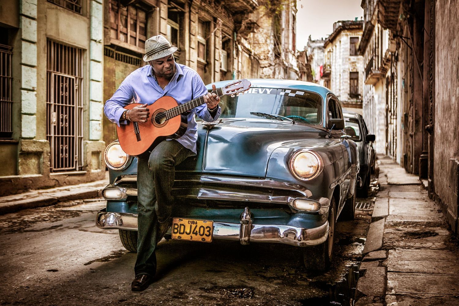 Adonis Puentes, photographed in Cuba playing guitar on an old car, photographer Alec Watson