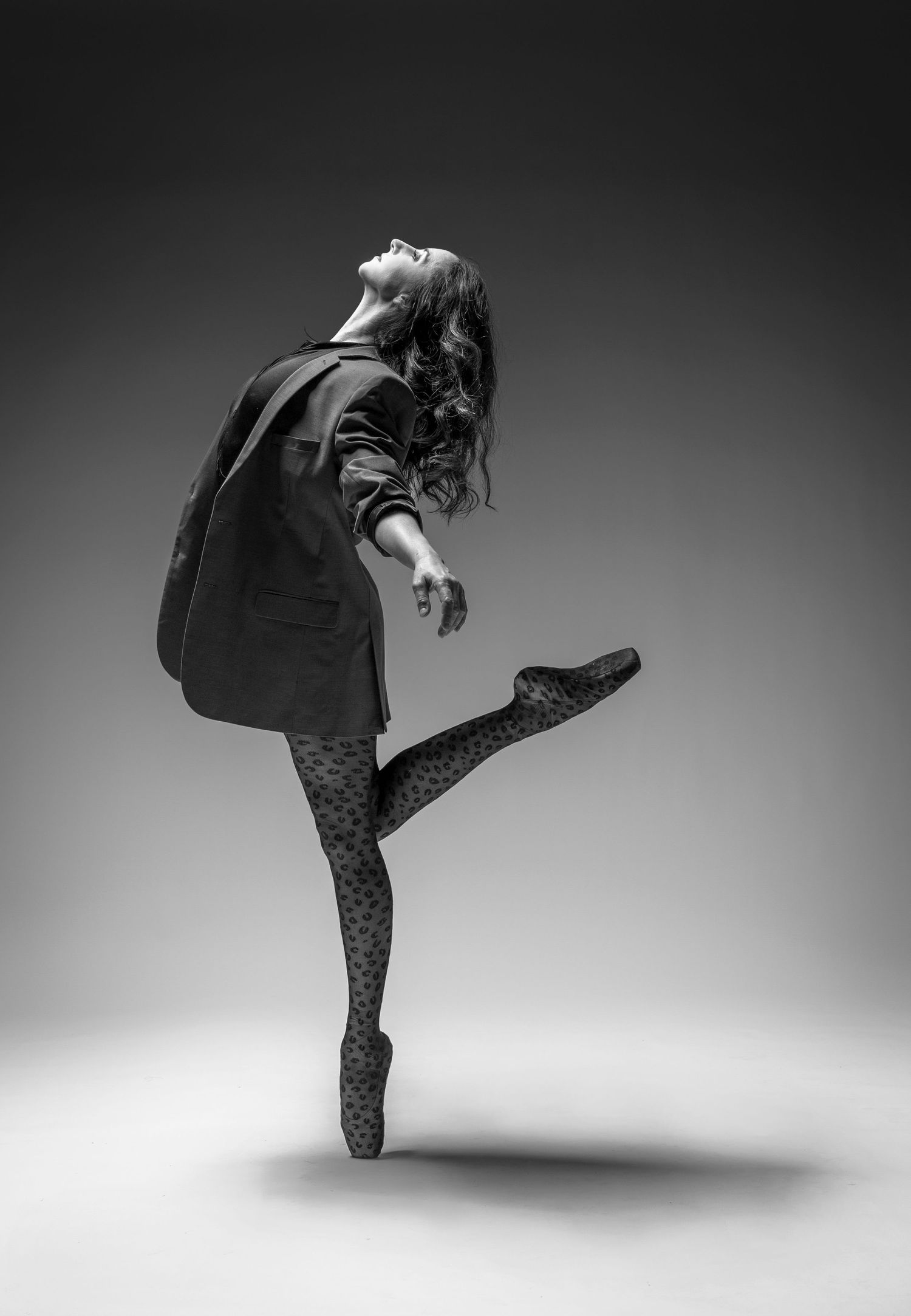 Black and white photo of a female dancer balancing on one foot with arms extended overhead, photographer Alec Watson
